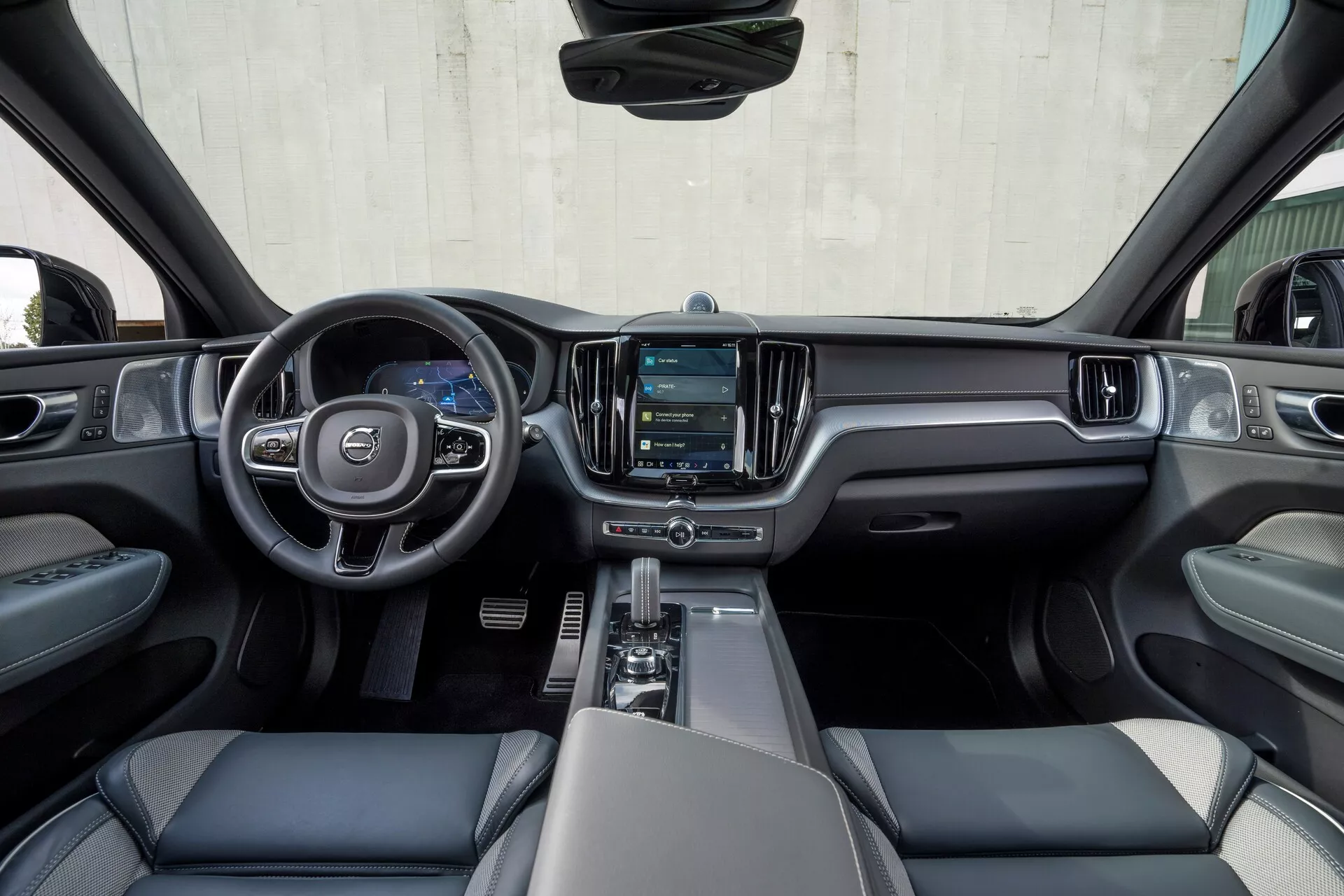 Vue intérieure depuis l'espace des sièges arrière d'une voiture moderne, montrant le tableau de bord avant, le volant, la console centrale et une partie des sièges conducteur et passager avant. Les caractéristiques incluent un volant multifonction à trois branches avec un emblème, un écran d'infodivertissement numérique, un sélecteur de vitesses, des porte-gobelets et des sièges avant rembourrés en cuir ou en matière similaire avec appuie-têtes. L'habitacle bien éclairé présente un schéma de couleur bicolore, combinant des plastiques souples, des accents métalliques et peut-être des options avancées de diagnostic et de divertissement automobile, indiquant un design et un confort automobile modernes.