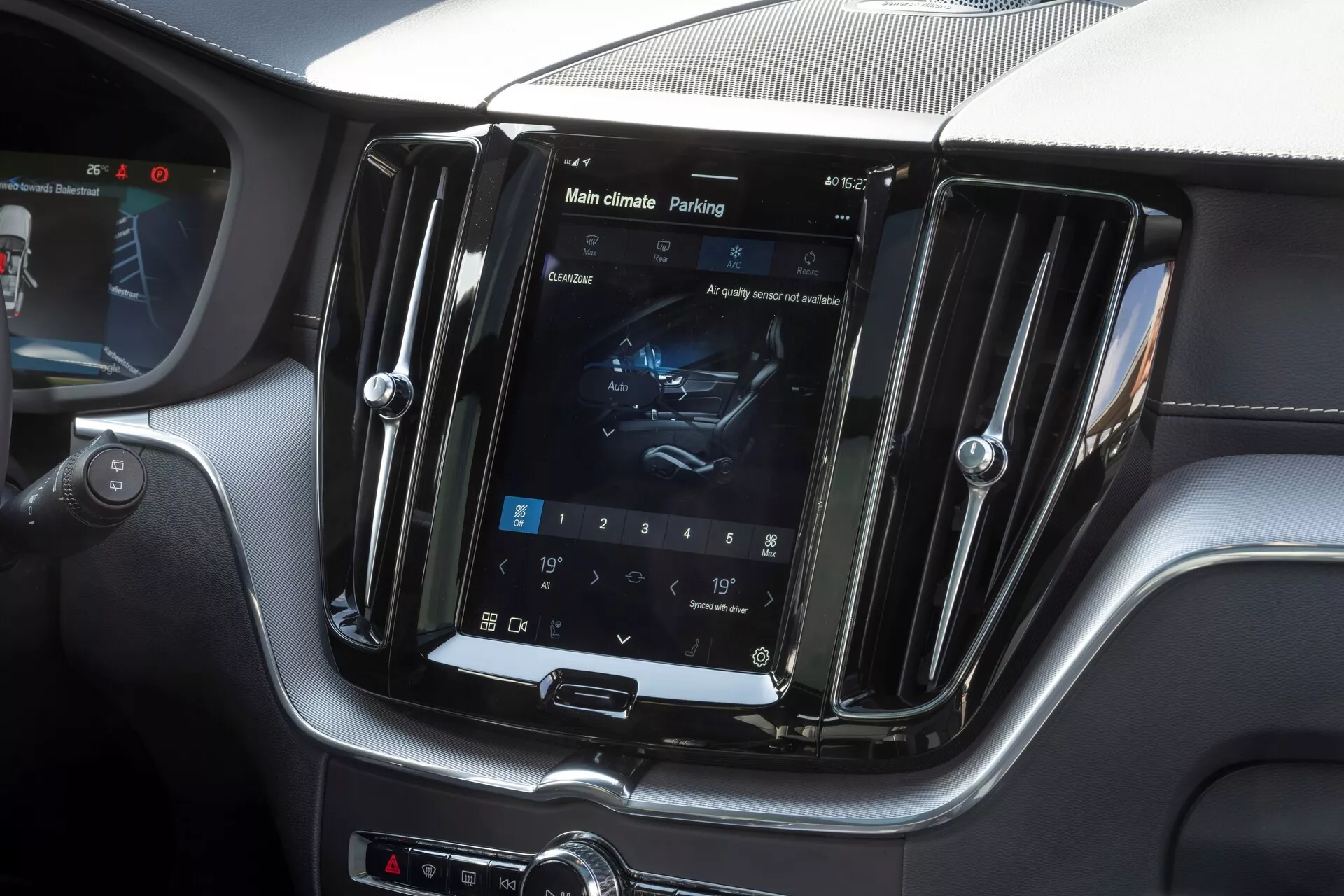 Photo intérieure de la Volvo XC60 2021 (restylage de la 2nde génération) axée sur la console centrale. L'image capture l'écran tactile d'infodivertissement verticalement orienté dans un boîtier semblable au chrome, affichant les réglages de commande du climat et un onglet d'assistance au stationnement. Un mélange luxueux de cuir et de finition en fibre de carbone entoure l'écran, avec une interface hybride comprenant des boutons physiques et des boutons de sélection. La photo met en évidence l'infodivertissement avancé, la commande du climat, l'assistance au stationnement et le design intérieur luxueux.