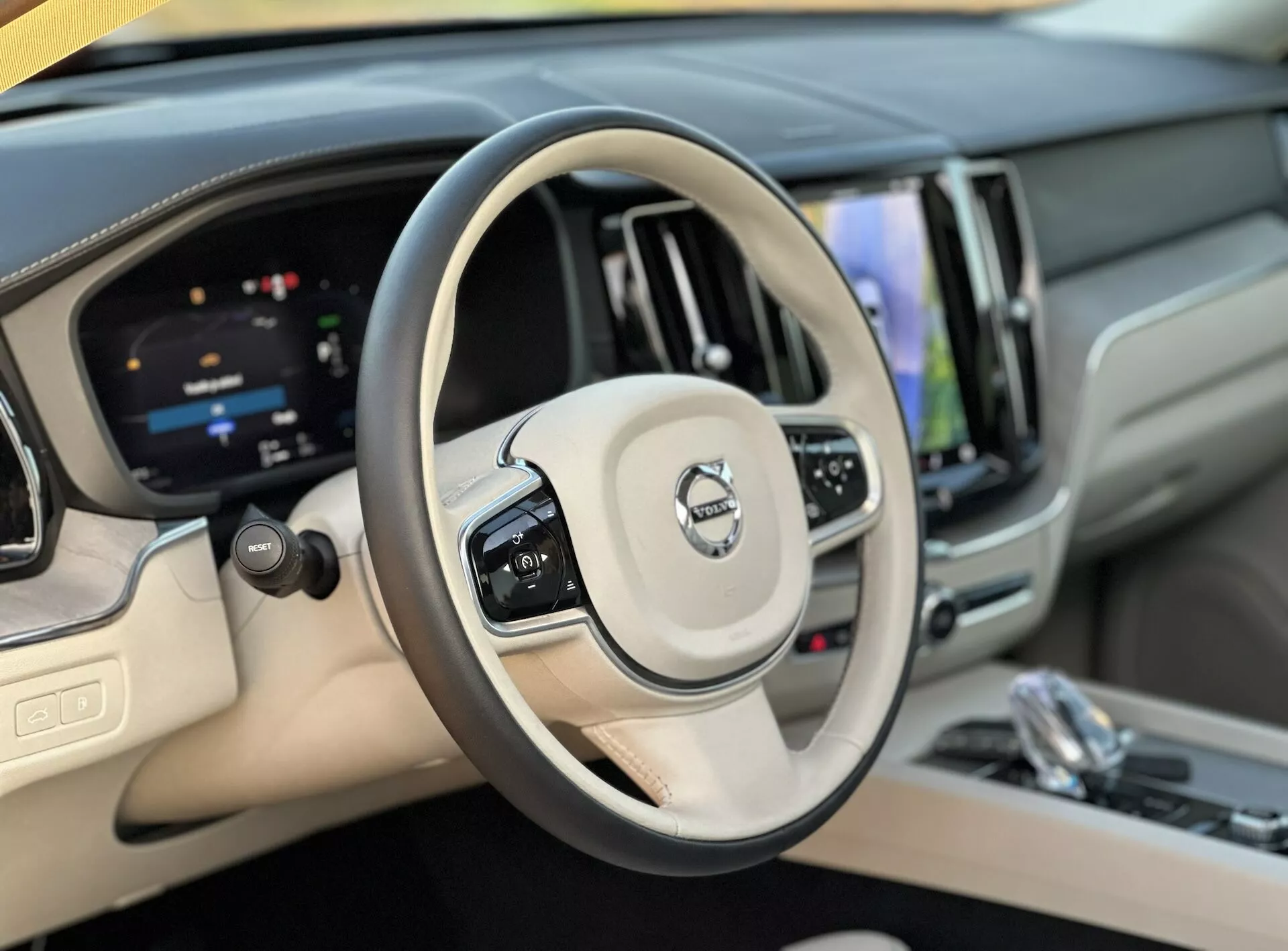 Vue intérieure du Volvo XC60 Recharge Plug-In Hybrid 2021 montrant le volant et le tableau de bord numérique depuis la perspective du conducteur, mettant en évidence le régulateur de vitesse, les boutons de gestion audio, un système d'infodivertissement tactile et des finitions de luxe