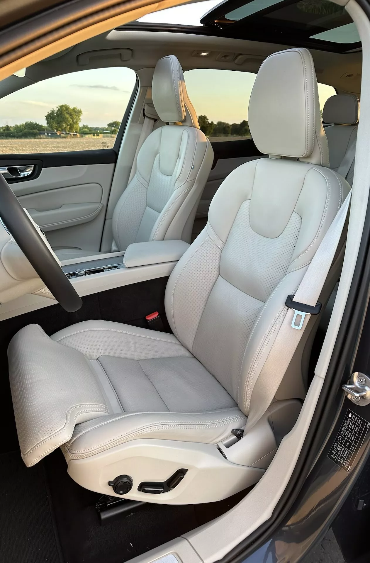 Vue intérieure du Volvo XC60 Recharge hybride branchable 2021 : sièges avant et aperçu des sièges arrière, sellerie en cuir luxueux de couleur claire, design moderne, sièges réglables électriquement avec lignes de couture élégantes, prise depuis l'extérieur de la porte côté passager en plein jour
