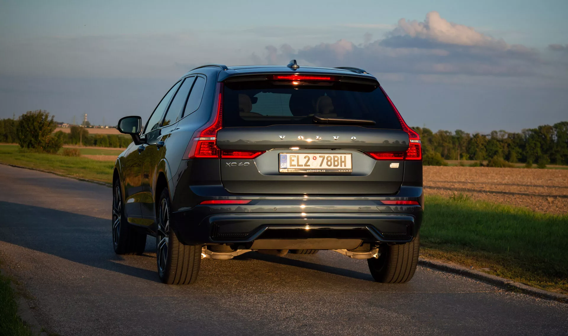 SUV Volvo XC60 Recharge hybride rechargeable 2021 sur route goudronnée, capturé sous un angle arrière de trois quarts mettant en évidence les feux arrière à LED du véhicule, le système d'échappement et les accents chromés en fin d'après-midi