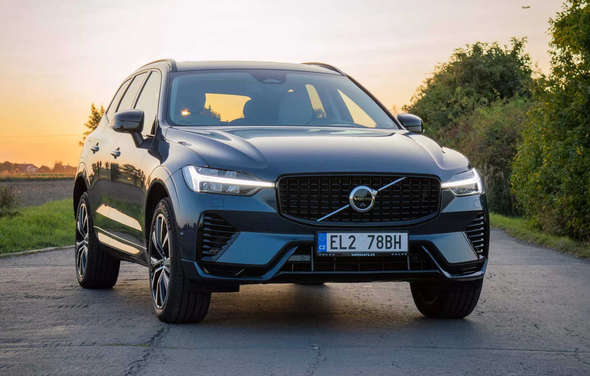SUV de luxe Volvo XC60 Recharge Plug-In Hybrid 2021 sur route pavée avec paysage naturel pendant l'heure dorée, présentant grille avant, phares LED, capot sculpté, roues en alliage à plusieurs branches et finition brillante