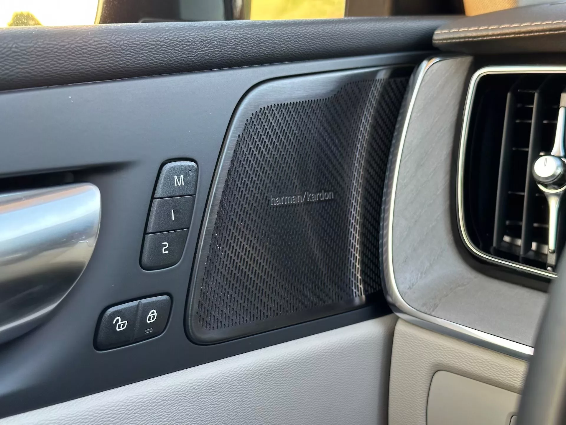 Vue intérieure du Volvo XC60 Recharge Plug-In Hybrid 2021 se concentrant sur le panneau de porte côté conducteur présentant les réglages de siège à mémoire, les commandes de verrouillage électronique des portes, une grille de haut-parleur harman/kardon et une partie de la grille d'aération du tableau de bord
