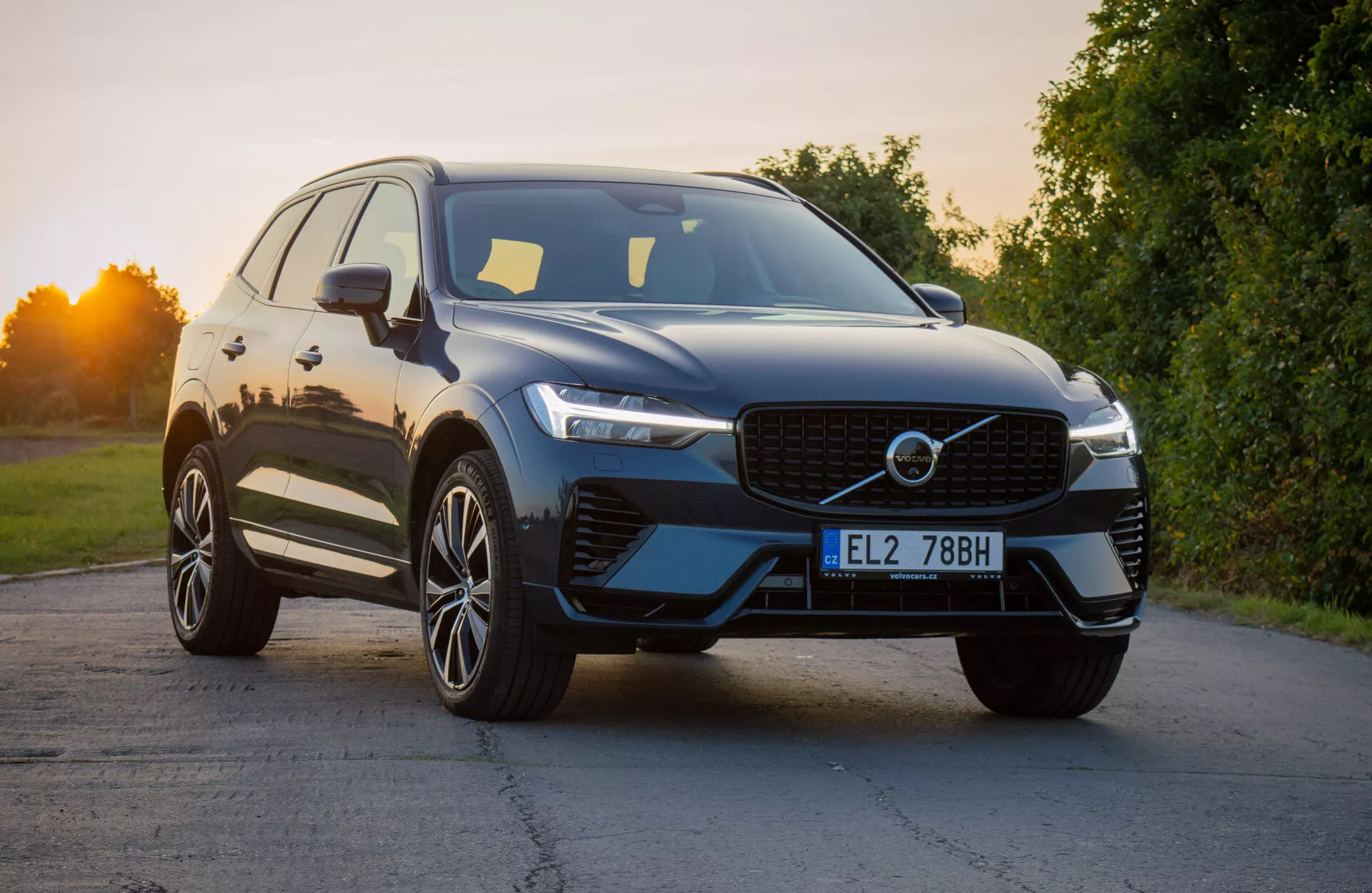 Volvo XC60 Recharge Plug-In Hybrid 2021 dans un design moderne de SUV positionné sous un léger angle pour mettre en avant le quart avant, montrant la grille distinctive, les phares LED élégants et le pare-chocs avant aérodynamique avec prises d'air intégrées, complété par une finition extérieure brillante et des roues en alliage à multi-branches sous la lumière naturelle du jour.