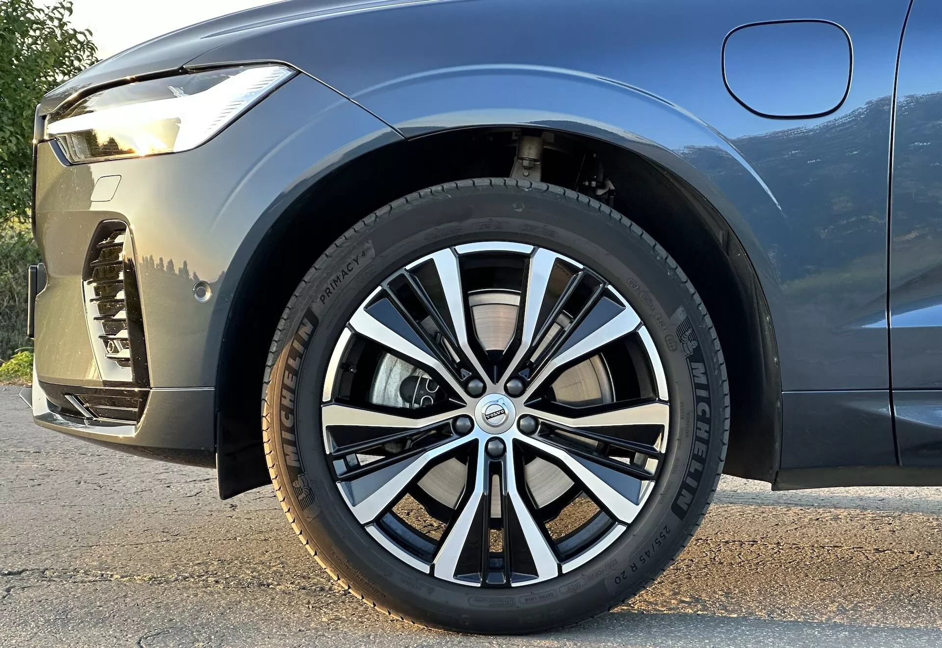 Vue rapprochée et en plongée de la Volvo XC60 Recharge Plug-In Hybrid 2021 sur la roue avant et une partie du corps latéral, mettant en évidence le design de la roue, la bande de roulement du pneu et la posture du véhicule