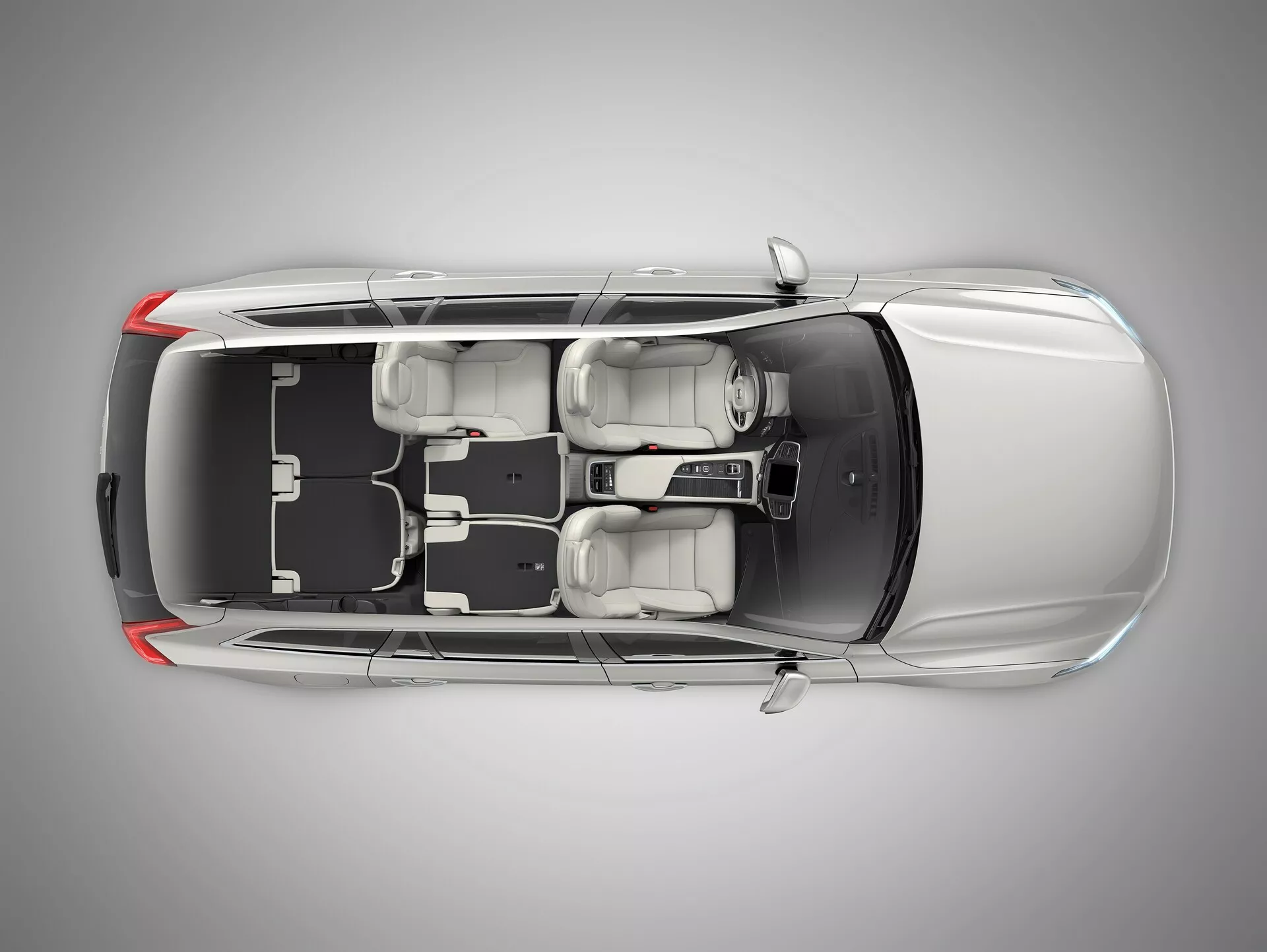 Vue d'oiseau d'une berline Volvo XC90 de deuxième génération de 2015 avec un toit transparent ou retiré numériquement, montrant l'intérieur. L'image révèle le long capot avant de la voiture, quatre portes fermées, quatre roues et la configuration des sièges avec deux sièges avant et une banquette arrière pour trois passagers. Console centrale et levier de vitesse visibles. Tableau de bord avec volant à gauche, écran et disposition des commandes montrés. Les éléments de design tels que les appuie-têtes, les rétroviseurs extérieurs et l'espace intérieur et sa disposition sont clairement visibles.