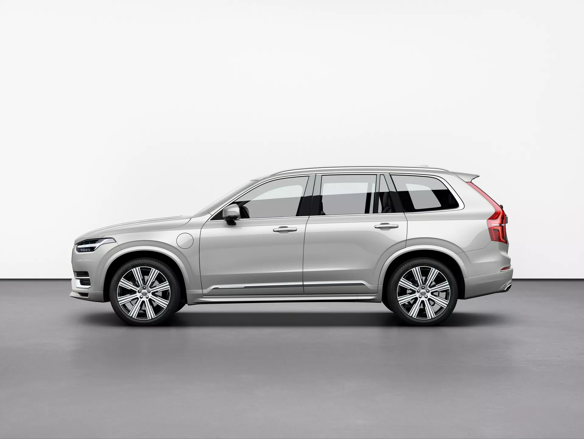 Image du SUV Volvo XC90 2015, photographié en vue trois-quarts avec un léger angle. Cette vue met en évidence les profils avant et latéral, montrant le design élégant et moderne de la voiture, les phares LED complexes, la calandre avant partiellement visible, les roues en alliage multi-branches, les rétroviseurs latéraux avec clignotants intégrés, les barres de toit, les lignes dynamiques de la carrosserie, la peinture et la couleur. L'éclairage doux dans le cadre du studio reflète avec précision les contours et les détails de surface du véhicule.
