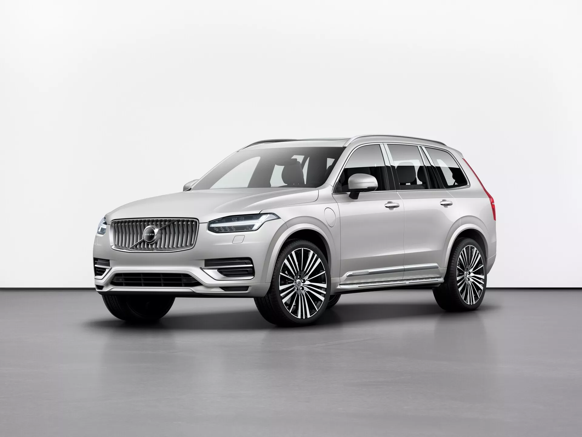 Photographie en studio d'un SUV de luxe Volvo XC90 2015 (2ème génération), représenté sous un angle avant trois-quarts, mettant en avant la calandre avec un logo distinctif, des phares LED élégants, un grand pare-chocs avant et un long empattement avec de grandes roues en alliage. Les rétroviseurs sont situés sous le pilier A, avec des fenêtres encadrées de garnitures chromées et des barres de toit. La couleur neutre de la peinture dégage une sophistication, et l'image met en valeur les lignes et contours du véhicule avec un éclairage uniforme sur un fond simple. Les caractéristiques probables incluent technologies d'assistance à la conduite et systèmes d'infodivertissement avancés.