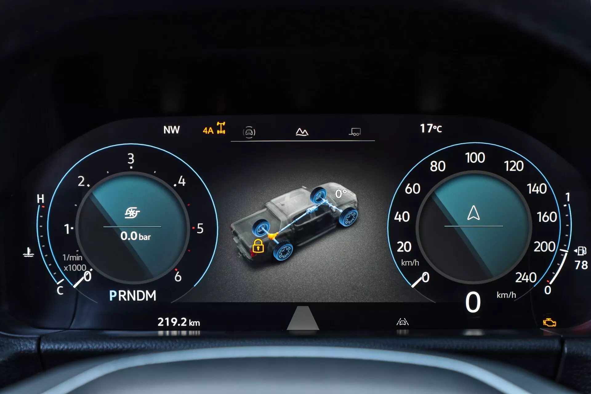 Vue détaillée du tableau de bord numérique de la deuxième génération du VW Nutzfahrzeuge Amarok 2023 depuis la perspective du conducteur. L'affichage numérique panoramique présente un design élégant avec un tachymètre et une jauge de carburant à gauche, un graphique central en 3D de la voiture pour la surveillance du système avec des indicateurs tels que la pression du turbo et l'état du groupe motopropulseur, et un compteur de vitesse à droite. Les éléments supplémentaires incluent un triangle d'avertissement, un indicateur de sélection de vitesse, un compteur de distance de voyage, direction de la boussole et température extérieure. L'image nette et bien éclairée se concentre sur l'affichage des caractéristiques technologiques avancées du véhicule à l'intérieur de l'habitacle, accentuée par le bord supérieur du volant.