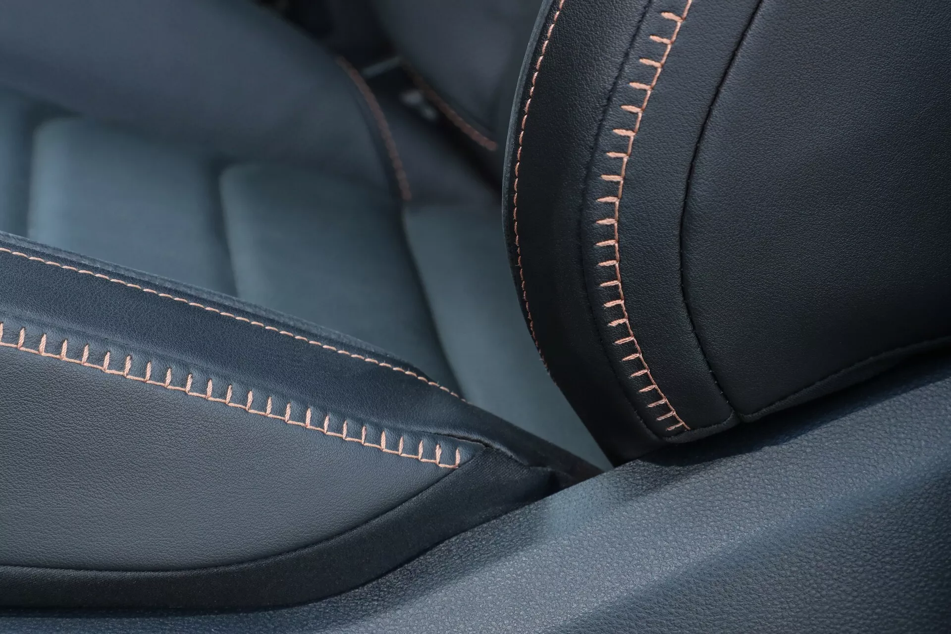 Gros plan détaillé de la sellerie en cuir du VW Nutzfahrzeuge Amarok 2023 (2e Génération), montrant un matériau de haute qualité avec une texture lisse et une finition mate. Les coutures oranges proéminentes et méticuleuses ajoutent une couleur de fil contrastante, soulignant le design et l'esthétique. L'angle oblique met en valeur la courbure et le confort ergonomique du siège. La faible profondeur de champ se concentre nettement sur les coutures, tandis que le reste se floute doucement. L'éclairage doux et diffus améliore la qualité du matériau sans reflets durs. Les tons sombres et le contraste orange créent une impression minimaliste et élégante, suggérant luxe et artisanat de haute qualité.