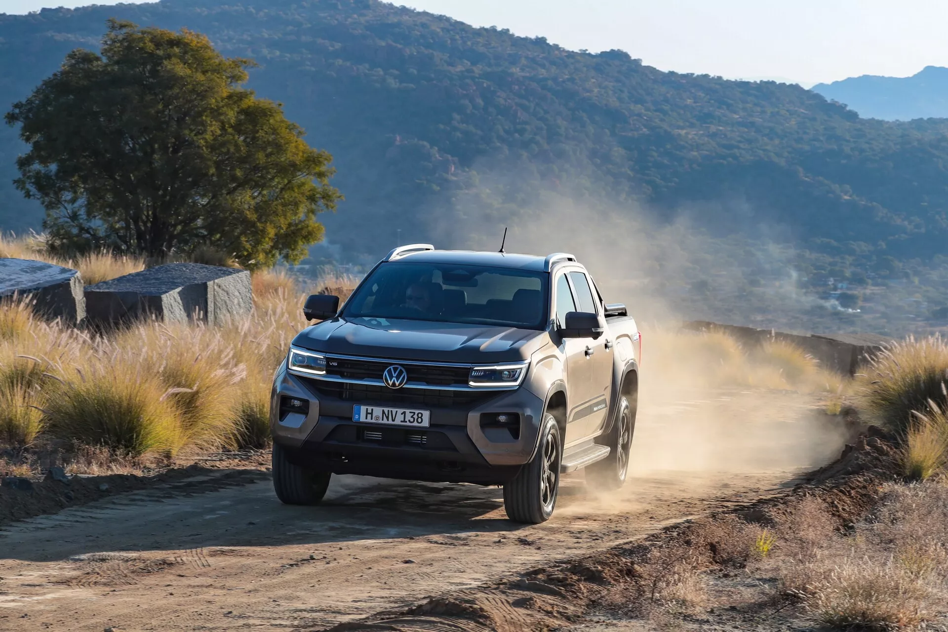 Pick-up moderne à double cabine roulant sur une route non pavée avec une traînée de poussière derrière, montrant sa robustesse et ses capacités tout-terrain. Le véhicule est capté sous un angle de trois quarts avant, mettant en avant la calandre avant, les phares avec technologie LED et le bord avant du capot. Les passages de roue avant et les roues sont en mouvement, indiquant un déplacement sur un terrain inégal. La traînée de poussière souligne ses performances en conditions tout-terrain. La photo transmet un sentiment des dimensions et de la posture du véhicule, avec un éclairage naturel diurne mettant en valeur ses détails.