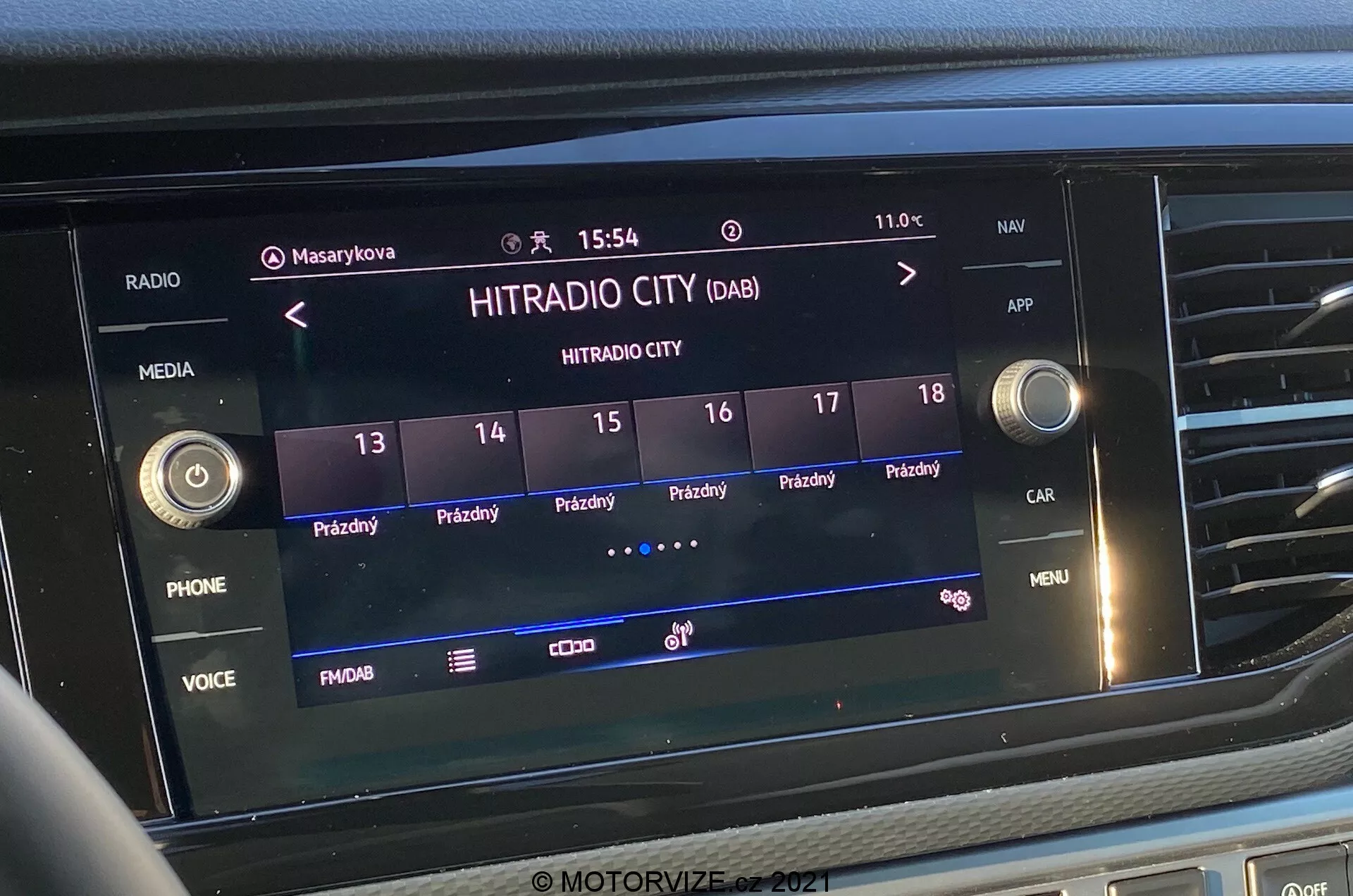 Gros plan frontal de l'écran du système d'infodivertissement du VW-Nutzfahrzeuge Transporter 2019 (T6-1 Multivan). L'image met en évidence la station de radio numérique 'HITRADIO CITY' sélectionnée, avec diverses options tactiles et des boutons de fonctions comme 'PHONE', 'VOICE' et 'MENU'. L'affichage indique l'heure '15:54' et la température extérieure '11.0°C', avec des icônes pour les profils utilisateurs, les réglages du véhicule et la puissance du signal. L'écran est intégré dans la partie centrale du tableau de bord, entouré de boutons tactiles et de commandes à boutons.