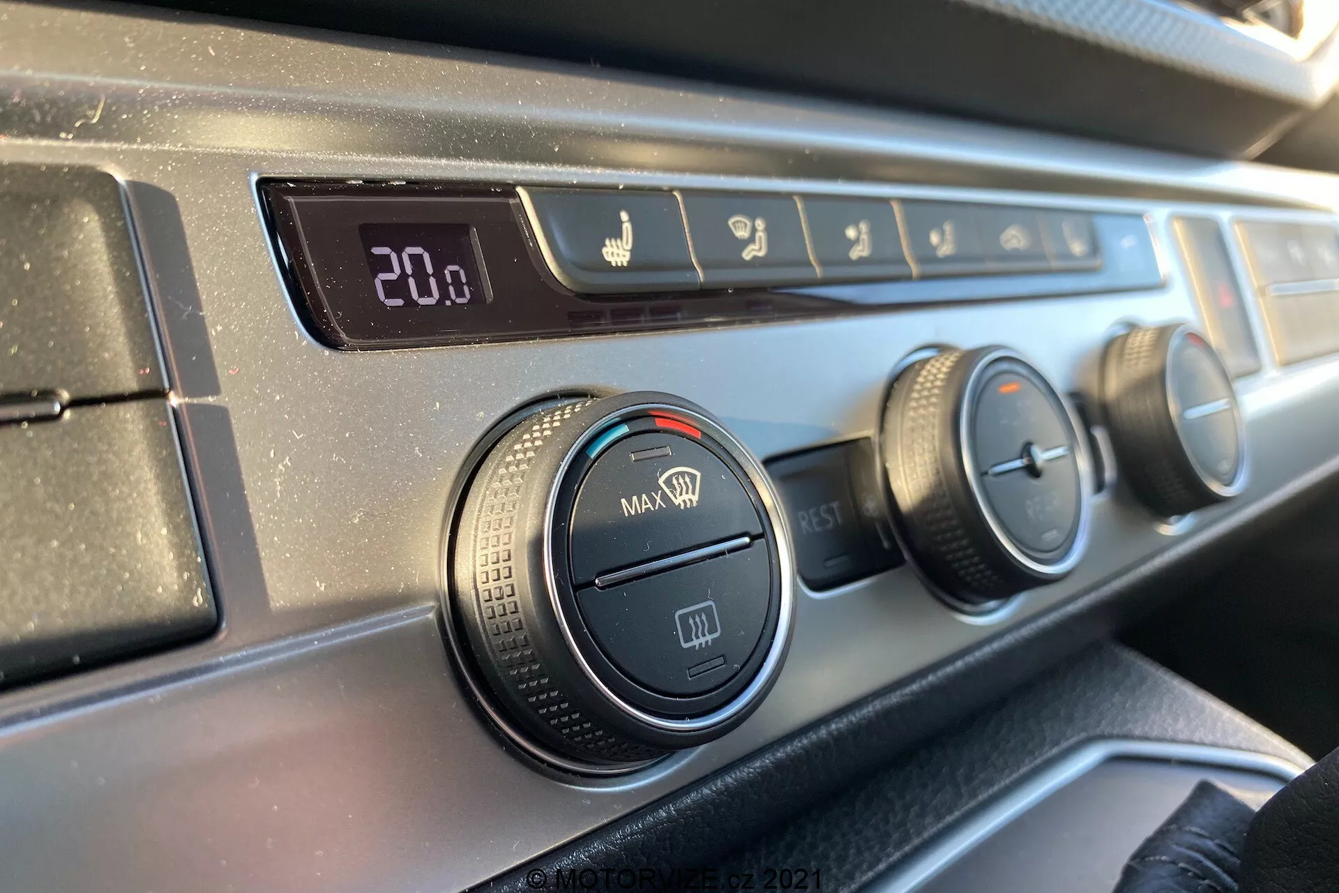 Vue rapprochée du panneau de contrôle du climat sur le tableau de bord du VW Transporter T6.1 Multivan 2019 depuis la perspective d'un occupant du siège avant, avec un affichage numérique de la température réglé à 20,0 degrés Celsius, des contrôles de direction du flux d'air, trois boutons rotatifs pour les réglages de la climatisation et du ventilateur, et un bouton de recirculation, le tout avec une bordure en plastique texturé noir et une finition lisse et sombre du tableau de bord.