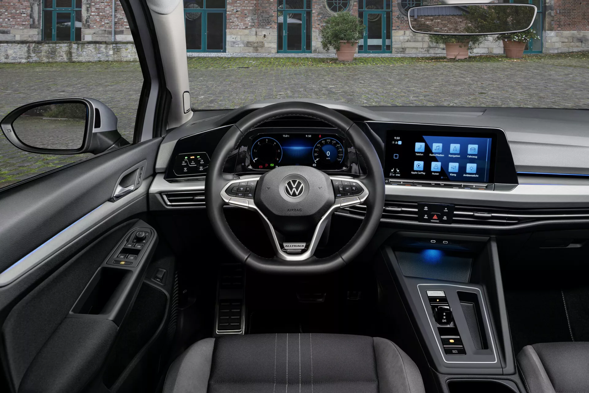 Vue intérieure d'une VW Golf Alltrack 2017 du point de vue du conducteur, présentant un volant à trois branches avec des commandes montées et le logo Volkswagen, un tableau de bord numérique et un large système d'infodivertissement tactile sur le tableau de bord, souligné par des caractéristiques technologiques avancées, des sièges garnis de cuir avec des coutures contrastées, et un mélange de matériaux de luxe et d'éclairage ambiance.