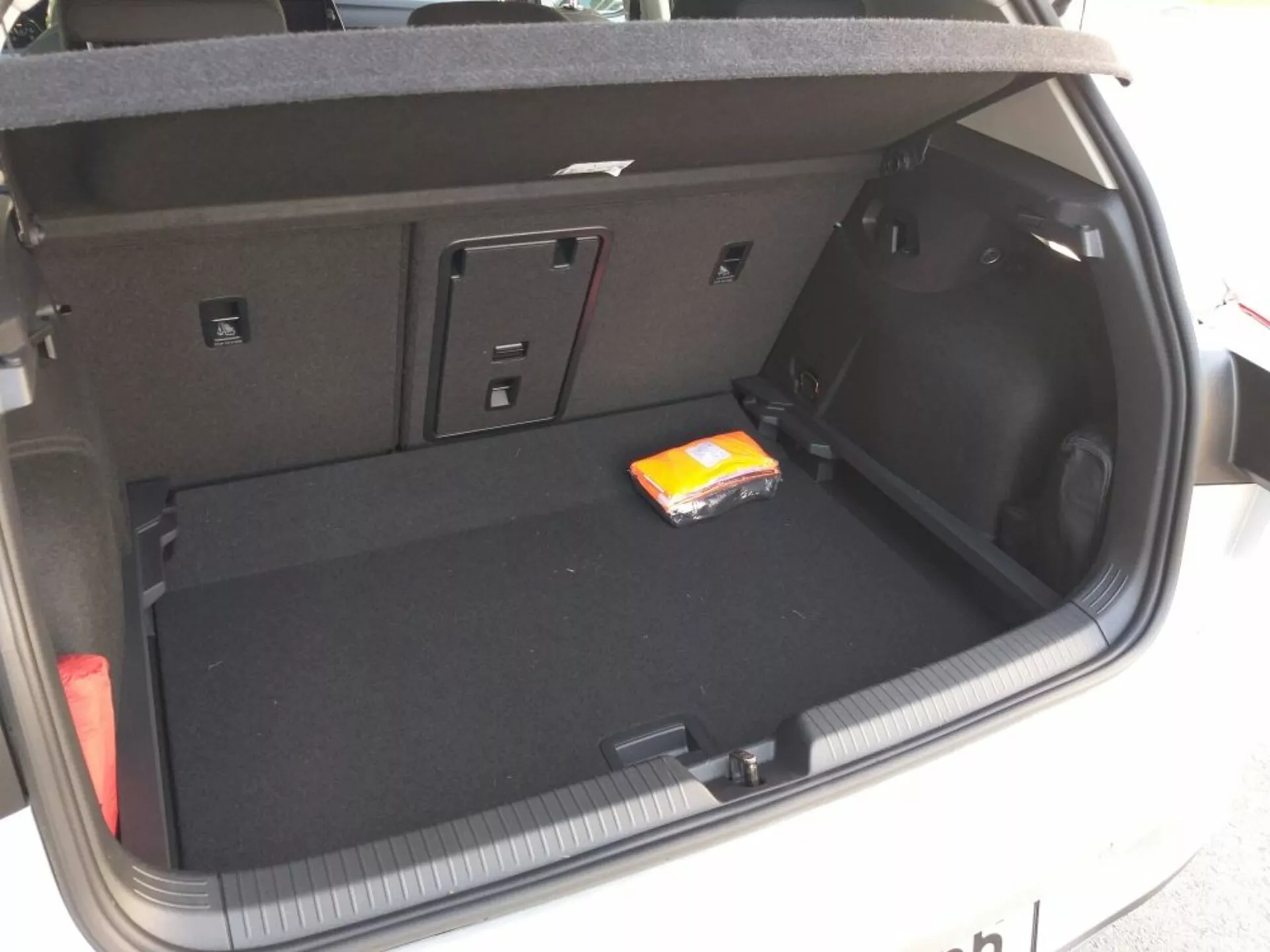 Coffre de la Volkswagen Golf GTD 2017 montrant l'aménagement et le design complets avec un revêtement de sol en moquette noire plate, espace de chargement principal vide avec un petit paquet de lingettes humides, compartiments latéraux pour petits objets ou équipement, accès aux sièges arrière rabattables pour espace supplémentaire, prise de 12V sur le côté droit, luminaire intégré dans le coffre et détails suggérant une opération d'ouverture/fermeture manuelle