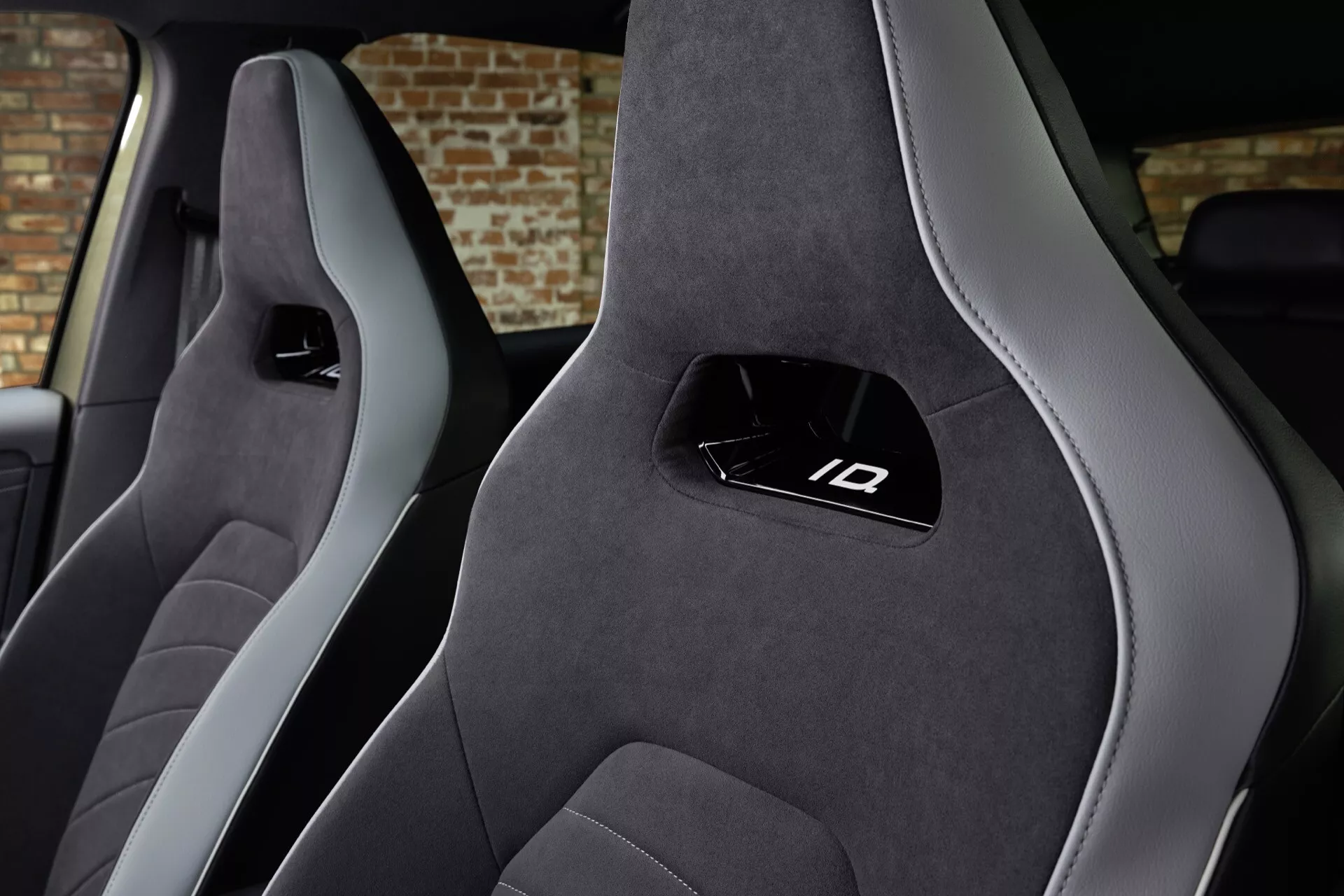 Intérieur du VW ID3 1ère Génération Facelift 2023 présentant des sièges baquets sport avant en couleur foncée et accents gris clair, appuie-têtes intégrés avec le logo ID, en suède ou Alcantara haut de gamme