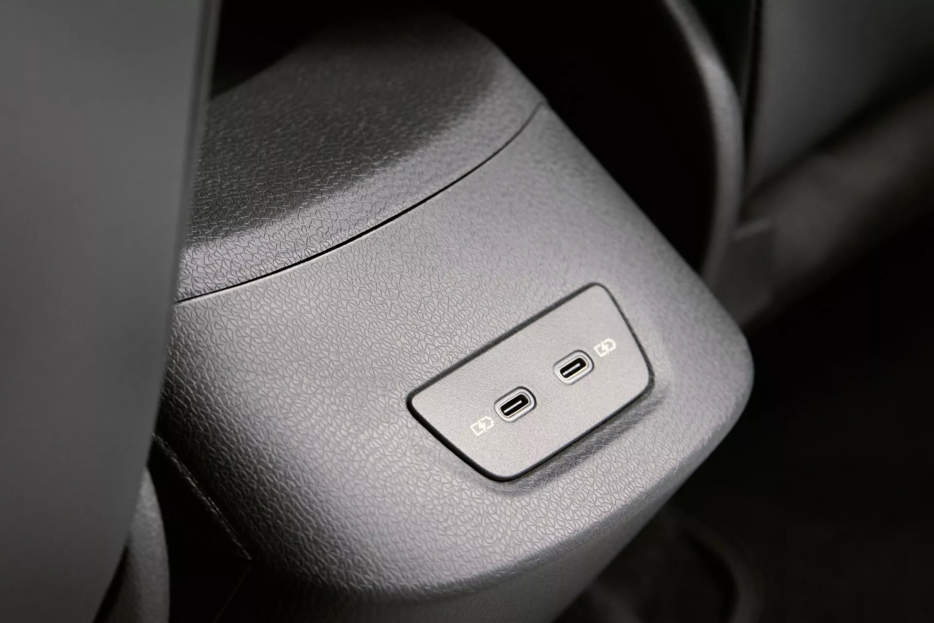 Gros plan de l'intérieur de la VW ID.3 2023 (1ère génération, restylée) montrant les boutons de réglage du siège sur le panneau de porte avec des symboles illuminés, une finition texturée et un design élégant et moderne