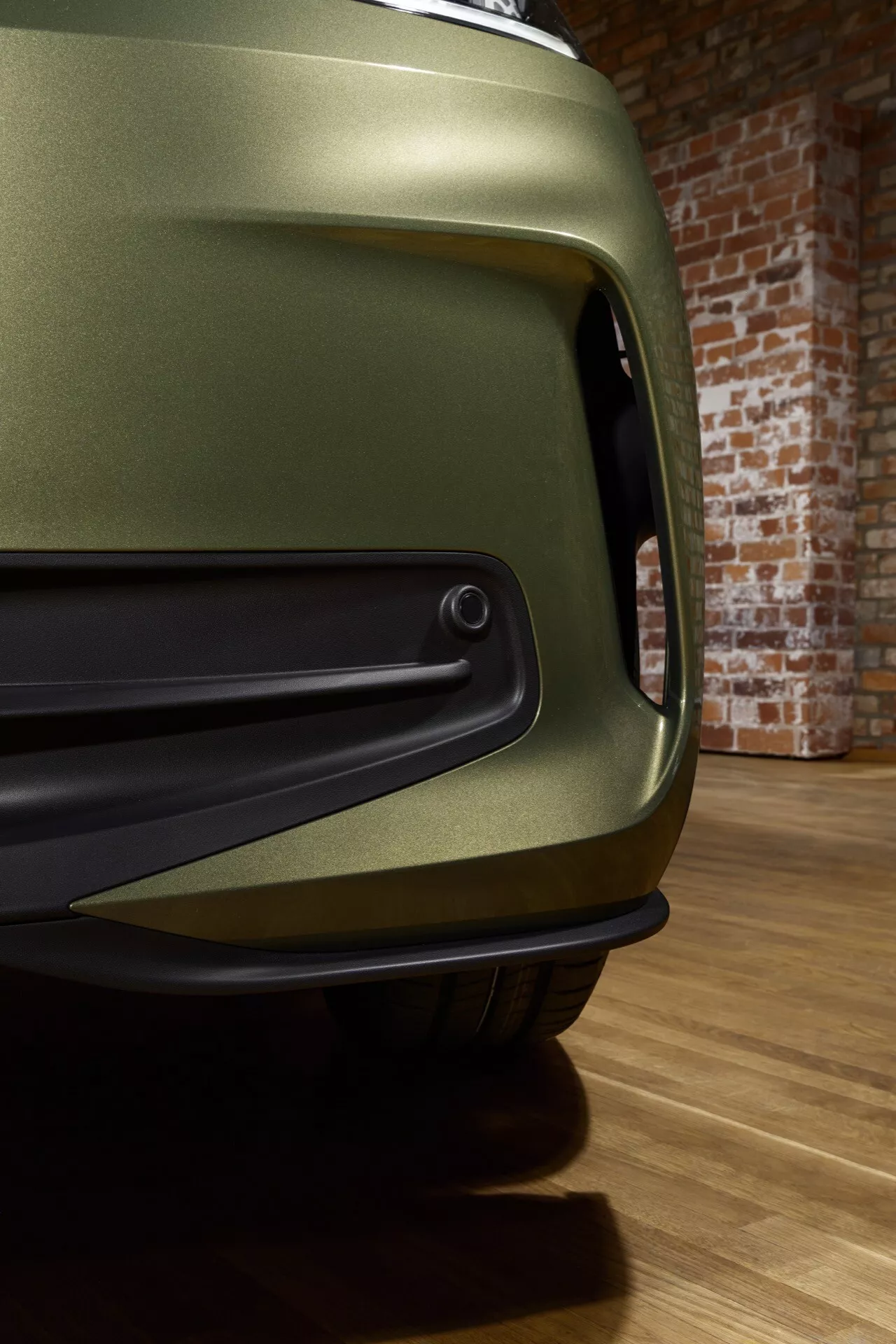 Vue rapprochée de la VW ID.3 1ère génération facelift de 2023 avec finition vert olive mat, se concentrant sur le pare-chocs avant aérodynamique et la prise d'air, capteur de stationnement intégré, dans un cadre de showroom mettant en évidence ses performances et détails de conception avancés.