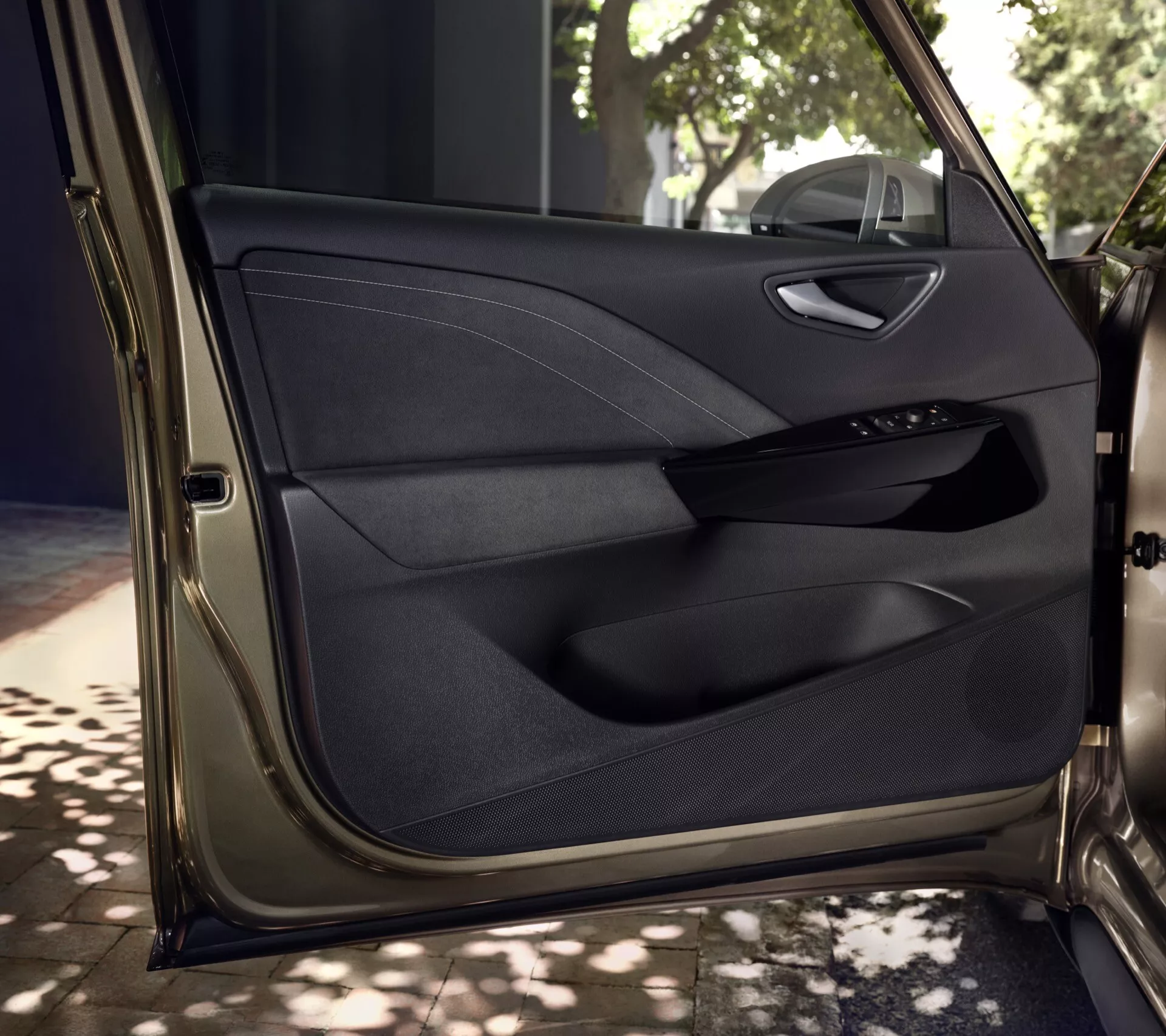 Vue détaillée de l'intérieur de la porte avant du conducteur de la VW ID.3 2023 1ère gen facelift, présentant un panneau de porte premium en multi-matériaux avec coutures, panneau de commande électronique pour les vitres et les miroirs électriques, poignée finie en chrome, compartiment de rangement et grille de haut-parleur intégrée sous éclairage naturel tacheté