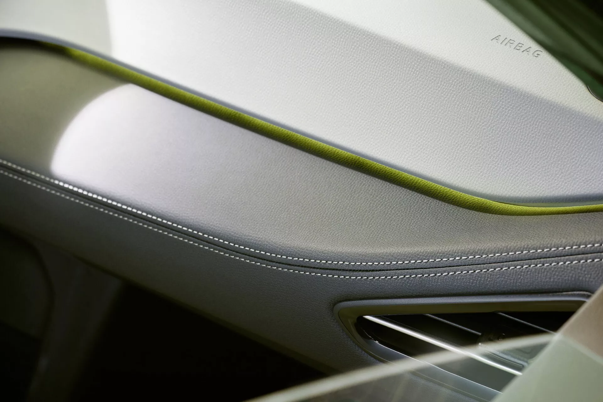 Gros plan sur l'intérieur du VW ID.3 2023 montrant une aération sur le tableau de bord ou le panneau de porte avec un accent en crème et vert lime, soulignant le savoir-faire de luxe, la fonction de sécurité avec AIRBAG en relief, et finition chromée pour un attrait haut de gamme