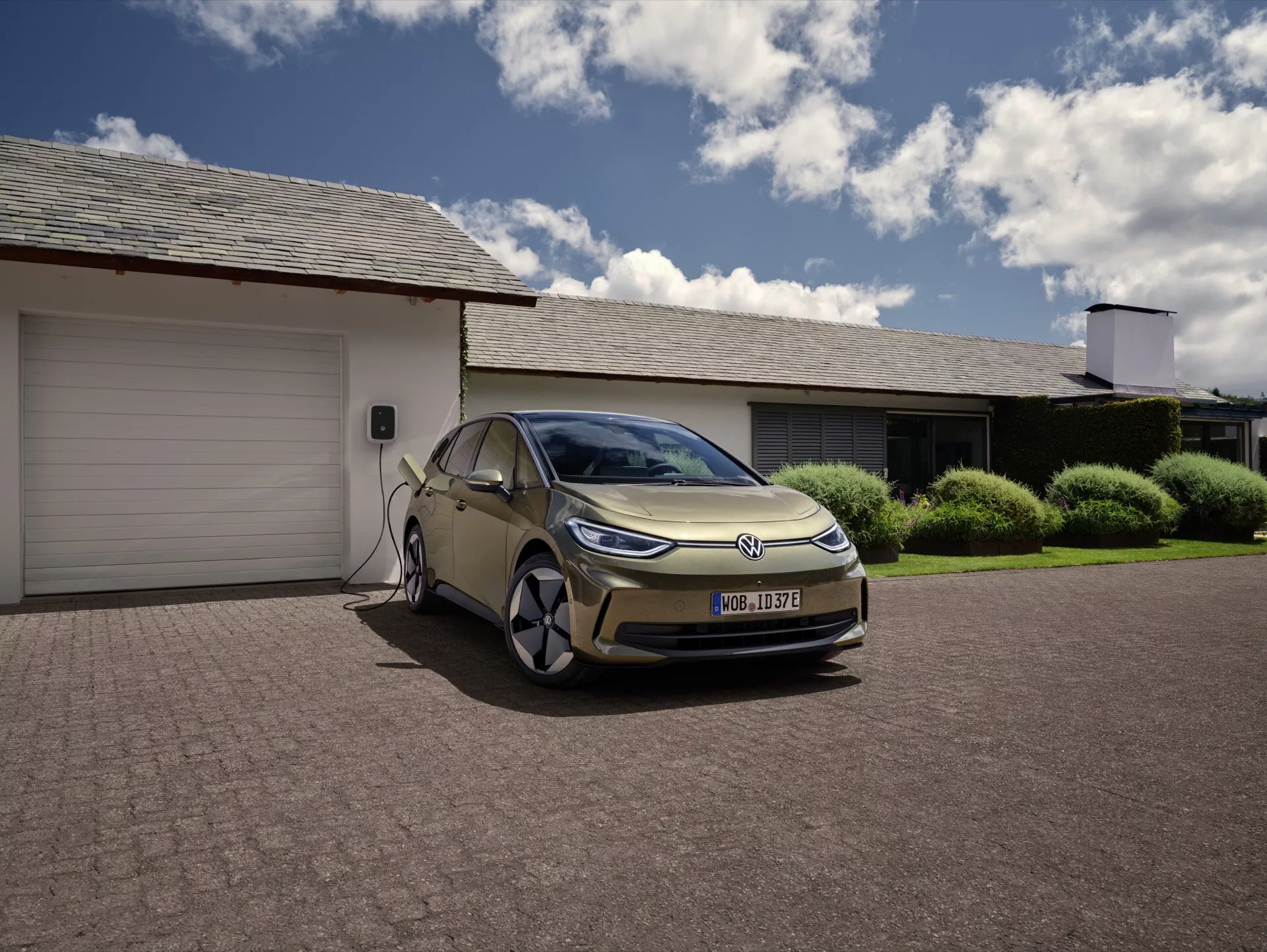 VW ID.3 1ère Génération Facelift véhicule électrique (EV) en charge à l'extérieur d'un garage résidentiel, montrant un design moderne avec des lignes épurées, des phares LED distinctifs, des caractéristiques aérodynamiques et la capacité de recharge à domicile, situé dans un cadre suburbain.