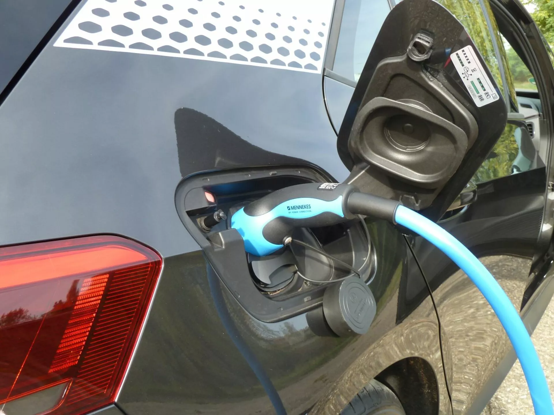 Vue rapprochée de la recharge d'une VW ID.3 électrique 2020, se concentrant sur le port de charge ouvert et le câble marqué Siemens sur le panneau arrière latéral de la voiture, avec un indicateur LED visible et des caractéristiques détaillées telles que le design moderne du feu arrière LED et la carrosserie brillante de couleur foncée.