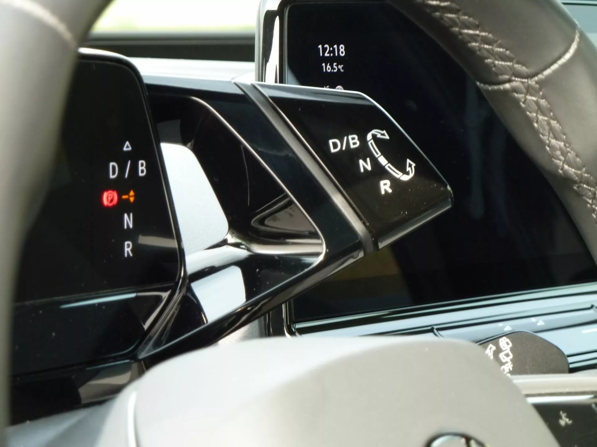 Intérieur du VW ID.3 2020 mettant en vedette la console centrale avec un gros plan sur le sélecteur de vitesse montrant les indicateurs des modes de conduite D/B et N/R, horloge digitale affichant 12:18 et température à 16,5°, soulignant la technologie moderne du véhicule et les éléments de design haut de gamme.