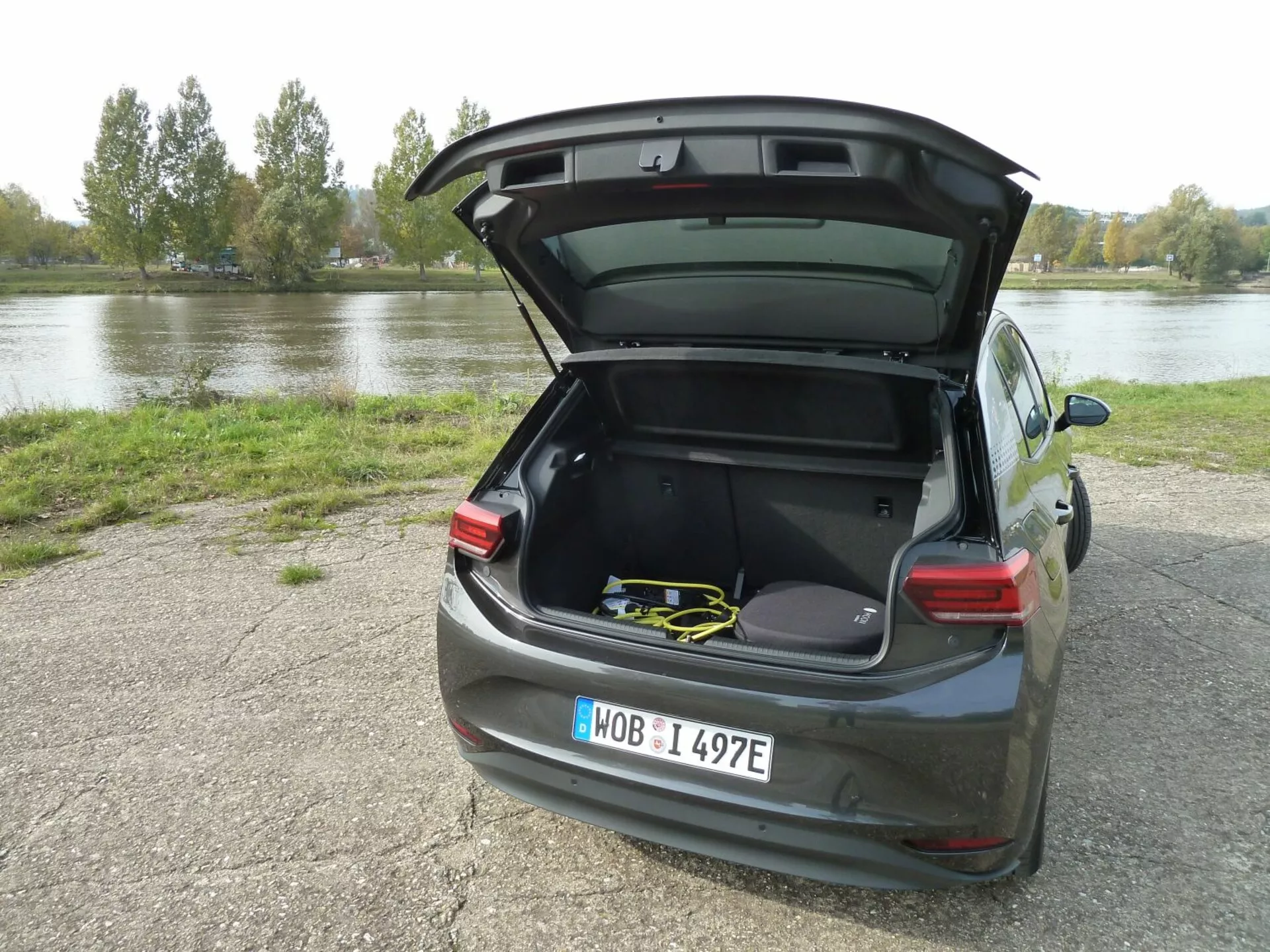 VW ID.3 de 2020 garée sur du gravier près de l'eau avec le coffre ouvert montrant un intérieur spacieux et du matériel de sport, vue arrière trois quarts