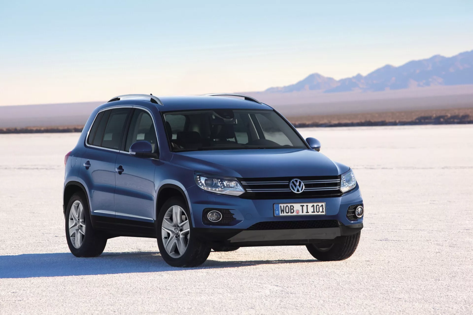 SUV Volkswagen Tiguan de 2007 sur un désert de sel sec, présentant sa vue frontale dynamique à trois quarts avec phares projecteurs, feux de brouillard, roues en alliage à multiples branches, clignotants intégrés dans les rétroviseurs latéraux, barres de toit et toit panoramique sous éclairage naturel