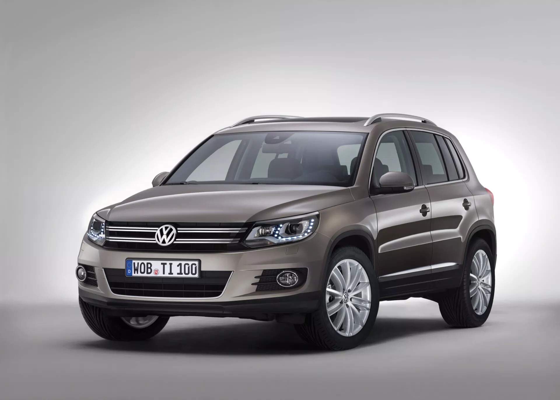 Image en studio du Volkswagen Tiguan 2007 présentant le côté avant gauche et le profil latéral sur un fond uni avec une ombre douce sous l'éclairage de studio, mettant en évidence la grille accentuée de chrome, les ensembles de phares élégants, les phares antibrouillard intégrés dans un garnissage noir, les roues en alliage à multiples branches, les rétroviseurs latéraux de couleur carrosserie avec clignotants intégrés et les barres de toit