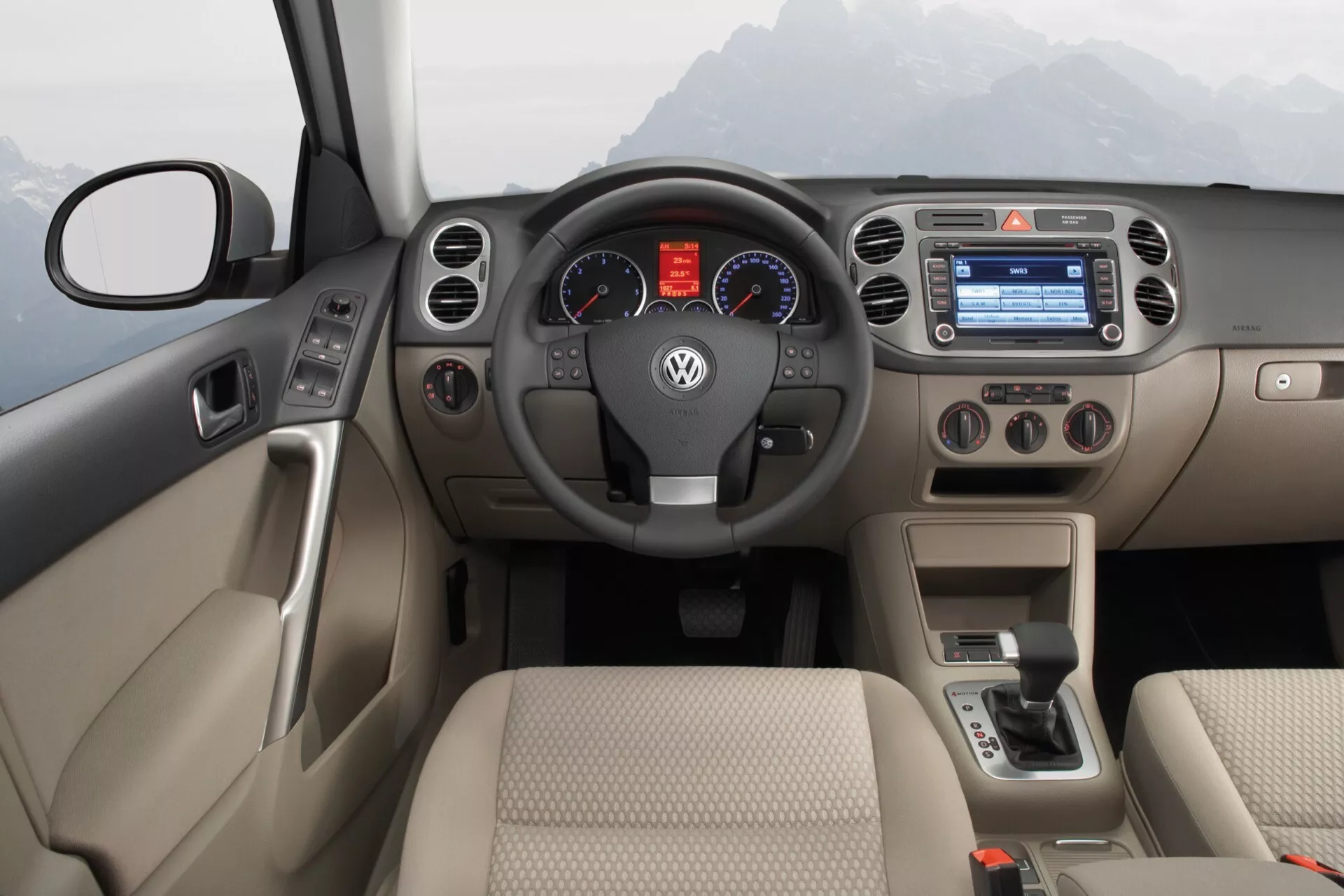 Intérieur du Volkswagen Tiguan 2007 montrant un tableau de bord bicolore, un volant multifonctions, un cluster d’instruments analogiques, un système multimédia avec écran couleur, des commandes manuelles de climatisation, et un levier de vitesse pour transmission automatique.