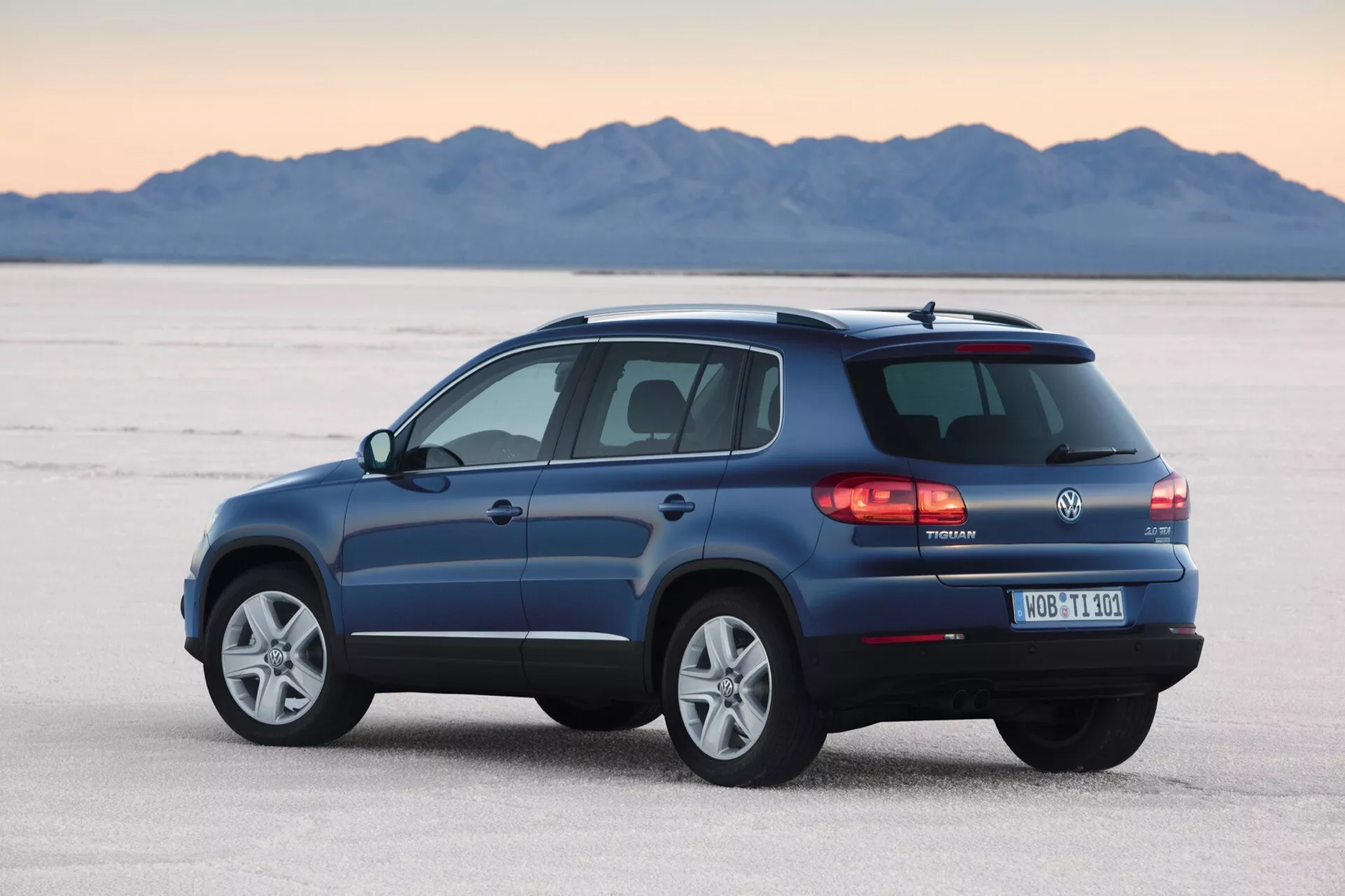 Volkswagen Tiguan 2007 en bleu métallique, présentant son design et ses caractéristiques depuis une vue arrière trois quarts sur un salar, avec des détails tels que feux arrière LED, essuie-glace arrière, barres de toit, jantes en alliage et pot d'échappement mis en évidence