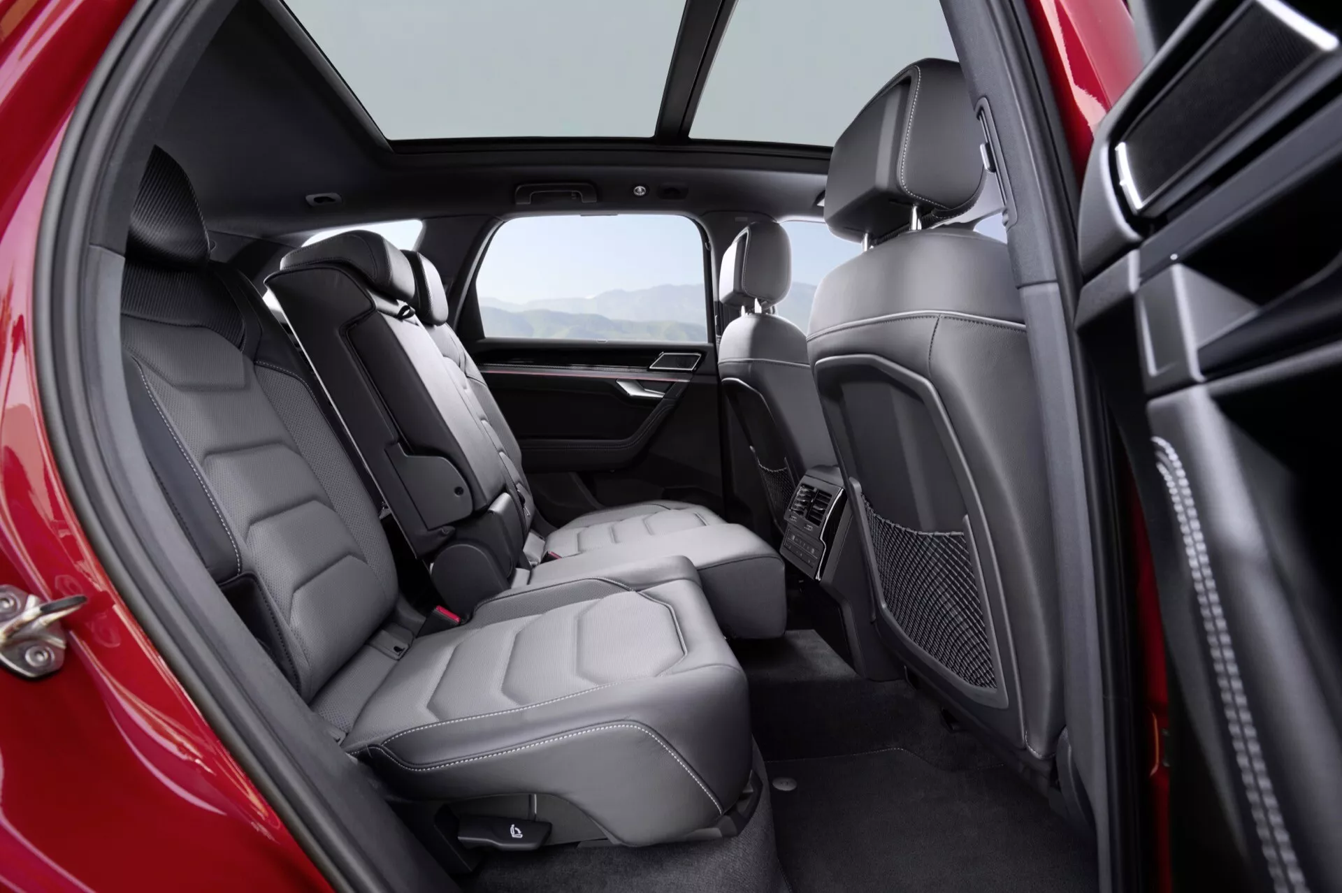 Vue intérieure du VW Touareg 2023 (III Facelift) centrée sur le compartiment des passagers arrière avec beaucoup d'espace pour les jambes, sièges en cuir et fonctionnalités de confort améliorées, incluant le contrôle du climat et l'éclairage d'ambiance