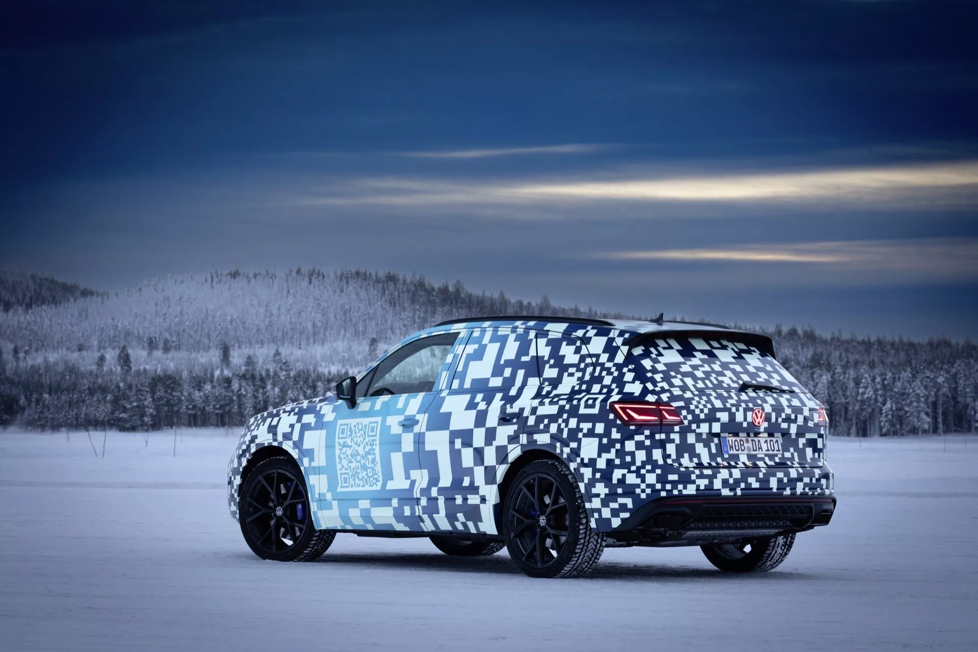 VW Touareg (III-facelift) 2023 de trois quarts arrière sur terrain enneigé avec enveloppe de camouflage, roues légères noires, feux arrières LED et spoiler suggérant une orientation performance