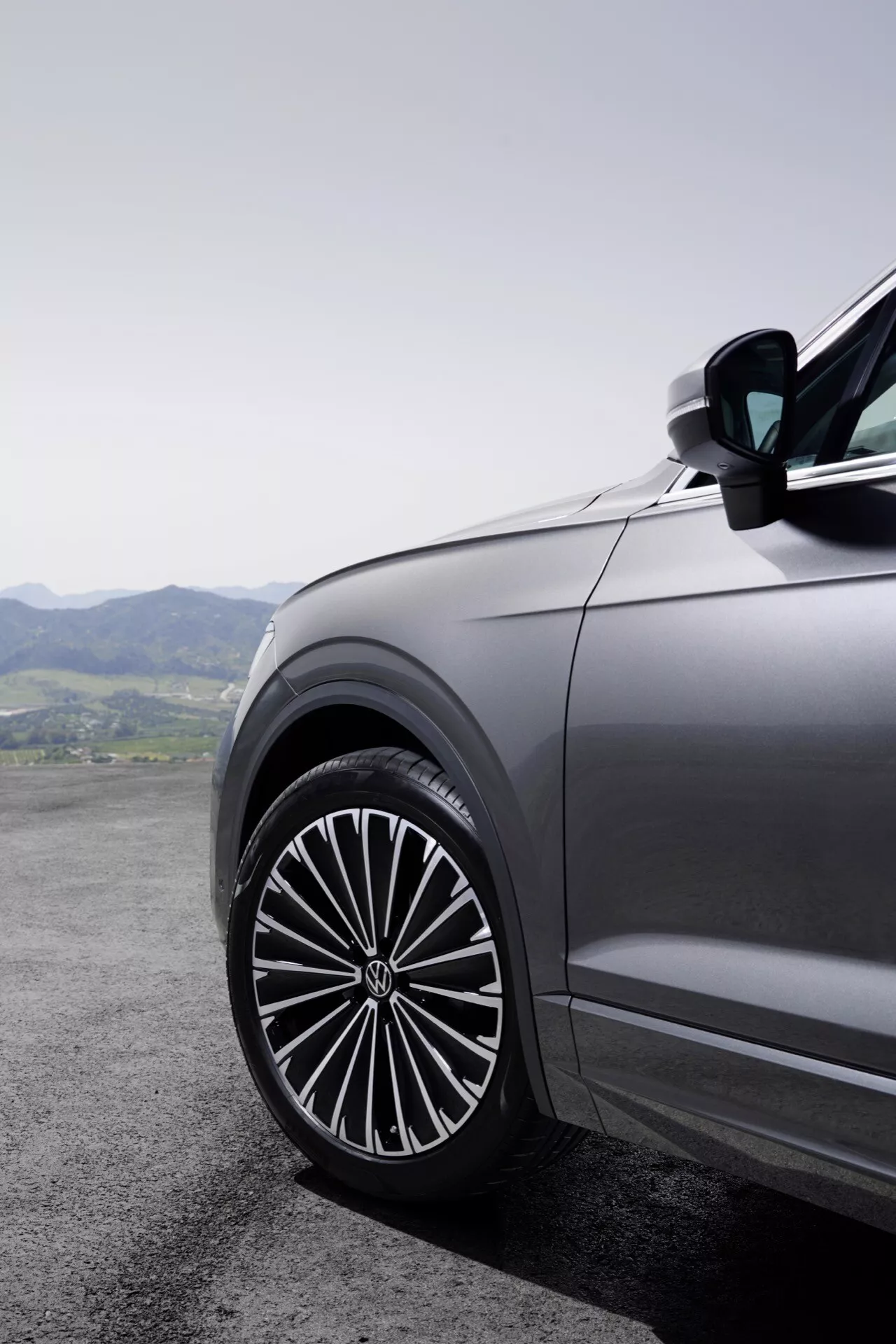 Vue rapprochée du quart avant côté conducteur de la Volkswagen Touareg 2023 (III Facelift) présentant une grande roue en alliage élégante avec un design à rayons multiples, reflétant la qualité d'un véhicule haut de gamme, sur un fond de paysage montagneux.