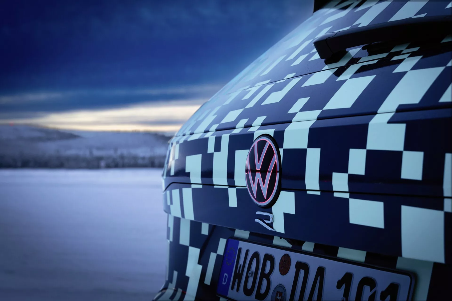 Vue rapprochée du quart arrière du Volkswagen Touareg (III Facelift) 2023 avec enveloppe de camouflage soulignant le montant C et l’emblème au crépuscule, mettant en avant les tests de prototypes automobiles et le design sous une lumière douce et froide