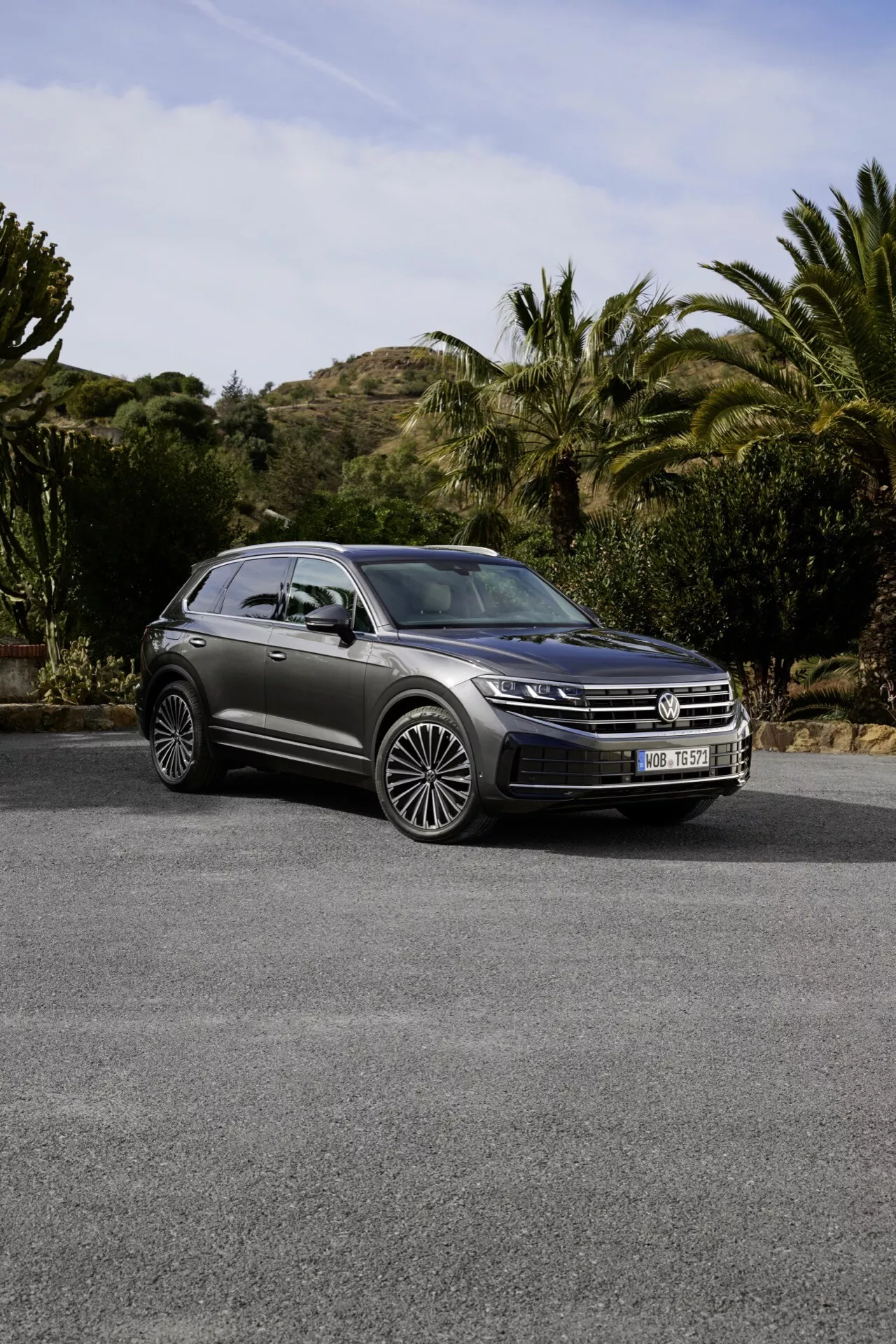 Modèle VW Touareg III facelift 2023 garé en extérieur avec calandre avant, phares LED, toit panoramique et jantes en alliage à multiples branches sur un fond de collines douces, d'arbustes et d'arbres, soulignant son design de SUV de luxe et ses caractéristiques avancées.