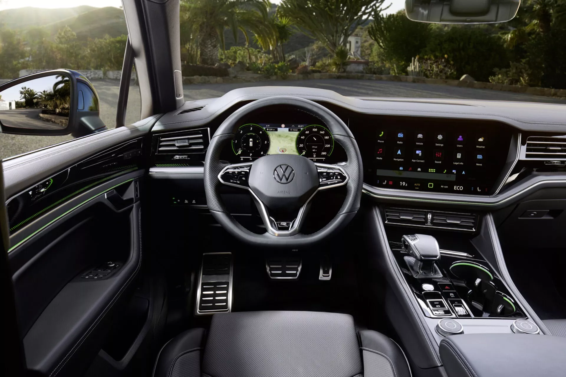 Vue intérieure du Volkswagen Touareg 2023 depuis le siège du conducteur montrant le volant avec commandes intégrées, tableau de bord numérique, système d'infodivertissement tactile, levier de vitesse élégant et garniture de qualité supérieure avec éclairage d'ambiance