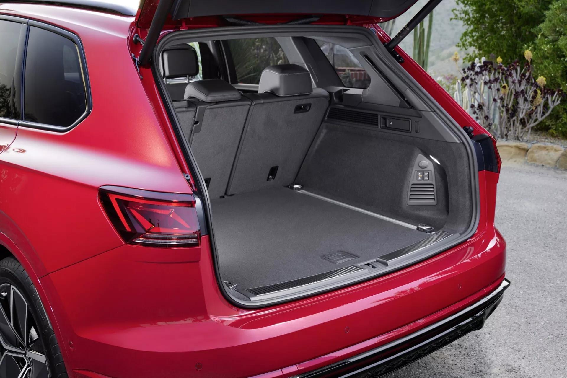 VW Touareg III Facelift 2023 montrant une vue détaillée de l'aire de chargement arrière spacieuse et riche en fonctionnalités du SUV rouge avec le hayon ouvert, y compris une vue partielle extérieure mettant en évidence les feux arrière LED et le design moderne