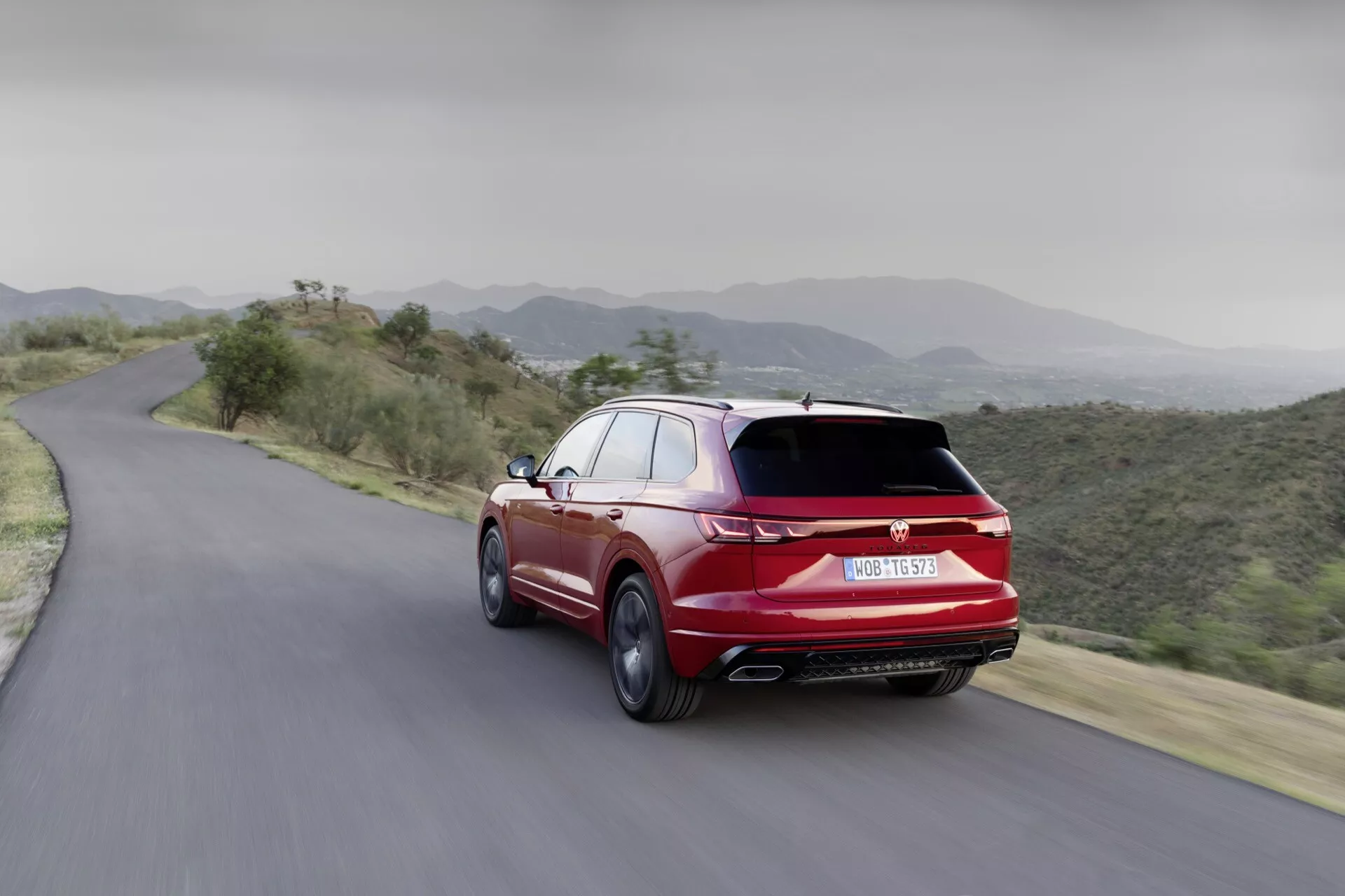Vue arrière dynamique du VW Touareg 2023 sur route de montagne, présentant un design aérodynamique, des échappements doubles et une finition sportive en rouge éclatant
