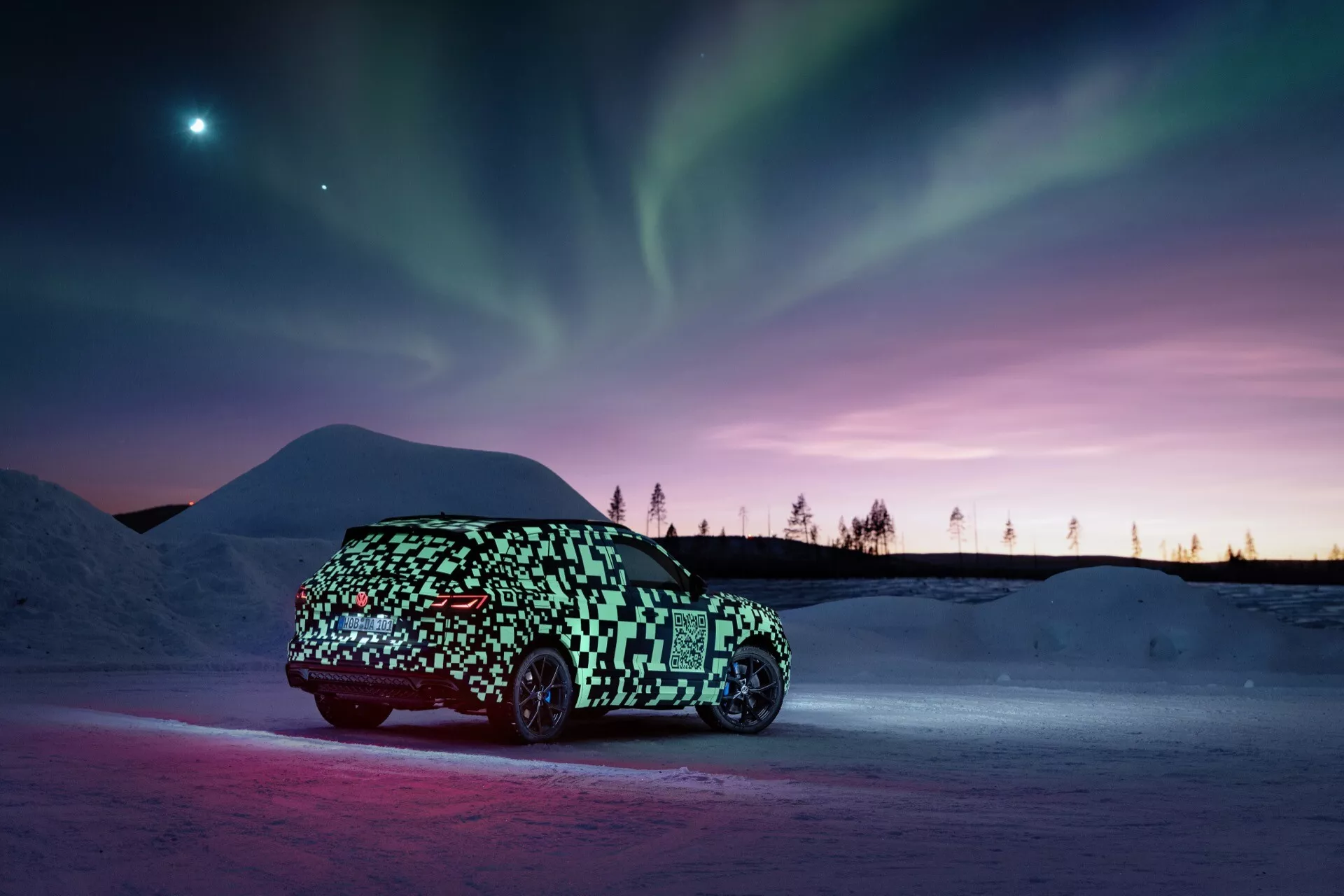 Prototype VW Touareg (III-Facelift) 2023 en camouflage capturé de profil sur un sol enneigé avec un éclairage ambiant soulignant le véhicule contre un arrière-plan d'aurore boréale et de teintes crépusculaires, suggérant un design élégant, peut-être électrique, de hatchback ou crossover