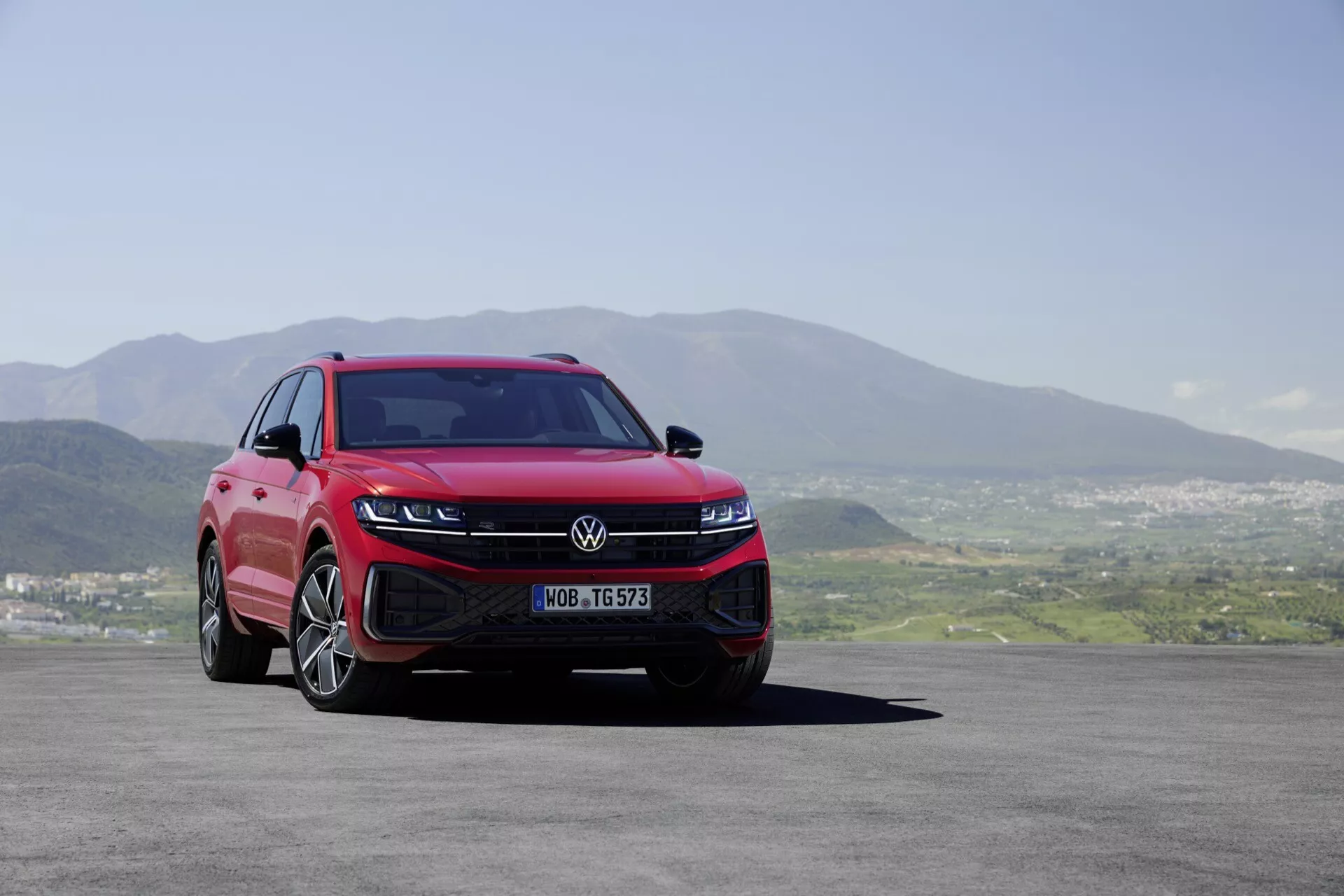 Volkswagen Touareg 2023 (III-Facelift) exposant son design moderne sous un angle avant bas de trois quarts mettant en lumière les phares LED, le pare-chocs avant sportif, la grille aérodynamique, et les jantes en alliage à multiples branches sur fond de paysage pittoresque.