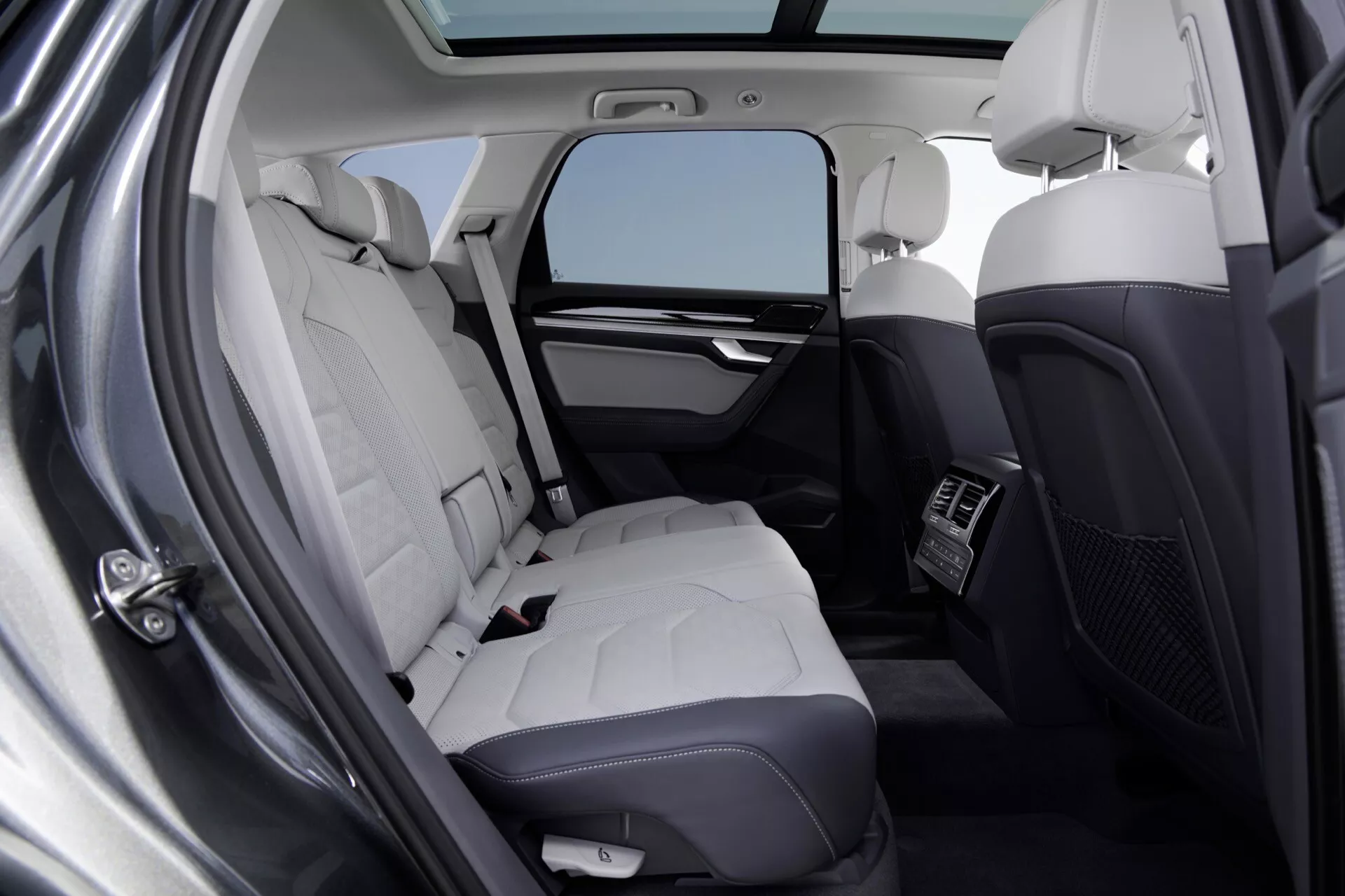 Vue intérieure du VW Touareg 2023 (III-Facelift) se concentrant sur la zone de sièges arrière de luxe avec des sièges en cuir de couleur claire, contrôle du climat et détails haut de gamme de la cabine depuis une perspective de la porte arrière gauche ouverte.