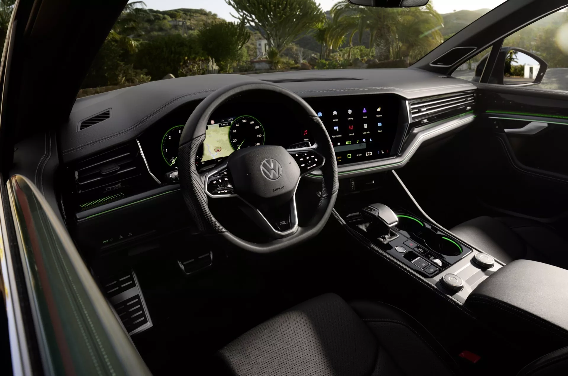 Vue intérieure du Volkswagen Touareg 2023 depuis le siège arrière, montrant le panneau de porte côté conducteur, siège conducteur ergonomique de première qualité, volant marqué Volkswagen avec commandes montées, tableau de bord numérique et grand système d'infodivertissement tactile avec navigation affichée, en plus de commandes climatiques minimalistes et sélecteur de transmission automatique dans la console centrale, reflétant des caractéristiques de luxe et de technologie avancée