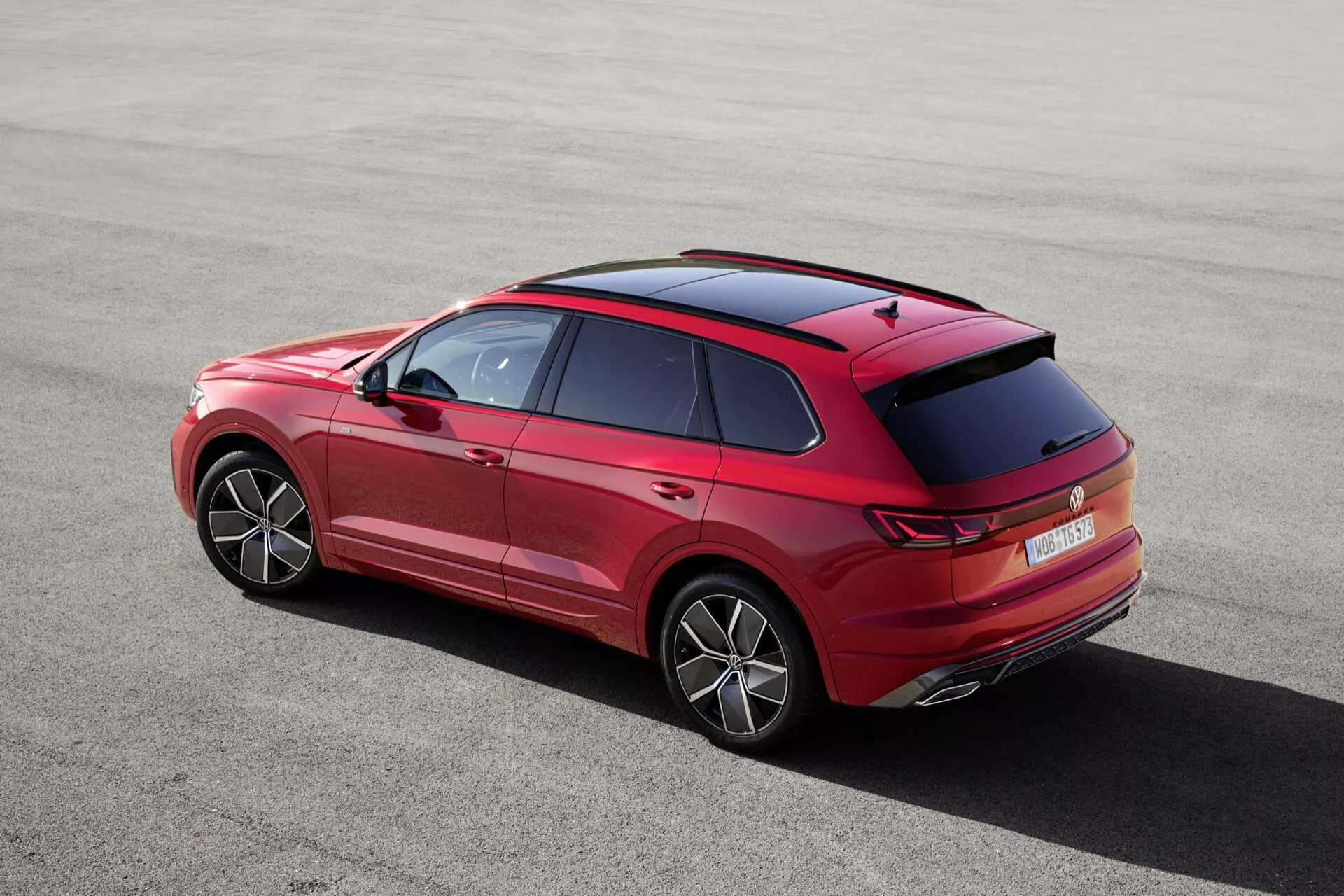 VW Touareg III facelift 2023 vu d'un angle arrière élevé de trois quarts montrant sa silhouette élégante, ses lignes de caractère distinctives, sa ligne de toit, son design détaillé du spoiler arrière et des antennes, la forme innovante des feux arrière et le design du pare-chocs, les roues visiblement claires avec des jantes stylisées, le pare-brise arrière, les éléments de design de la porte arrière avec poignées et moulures, avec des indices de la porte avant et des rétroviseurs latéraux, présentant des caractéristiques technologiques telles que les capteurs de stationnement arrière, la lumière de freinage haute, la technologie lumineuse LED ou OLED des feux arrière, et éventuellement des ajouts aérodynamiques sur le pare-chocs arrière, accentuant les proportions et la posture du véhicule.