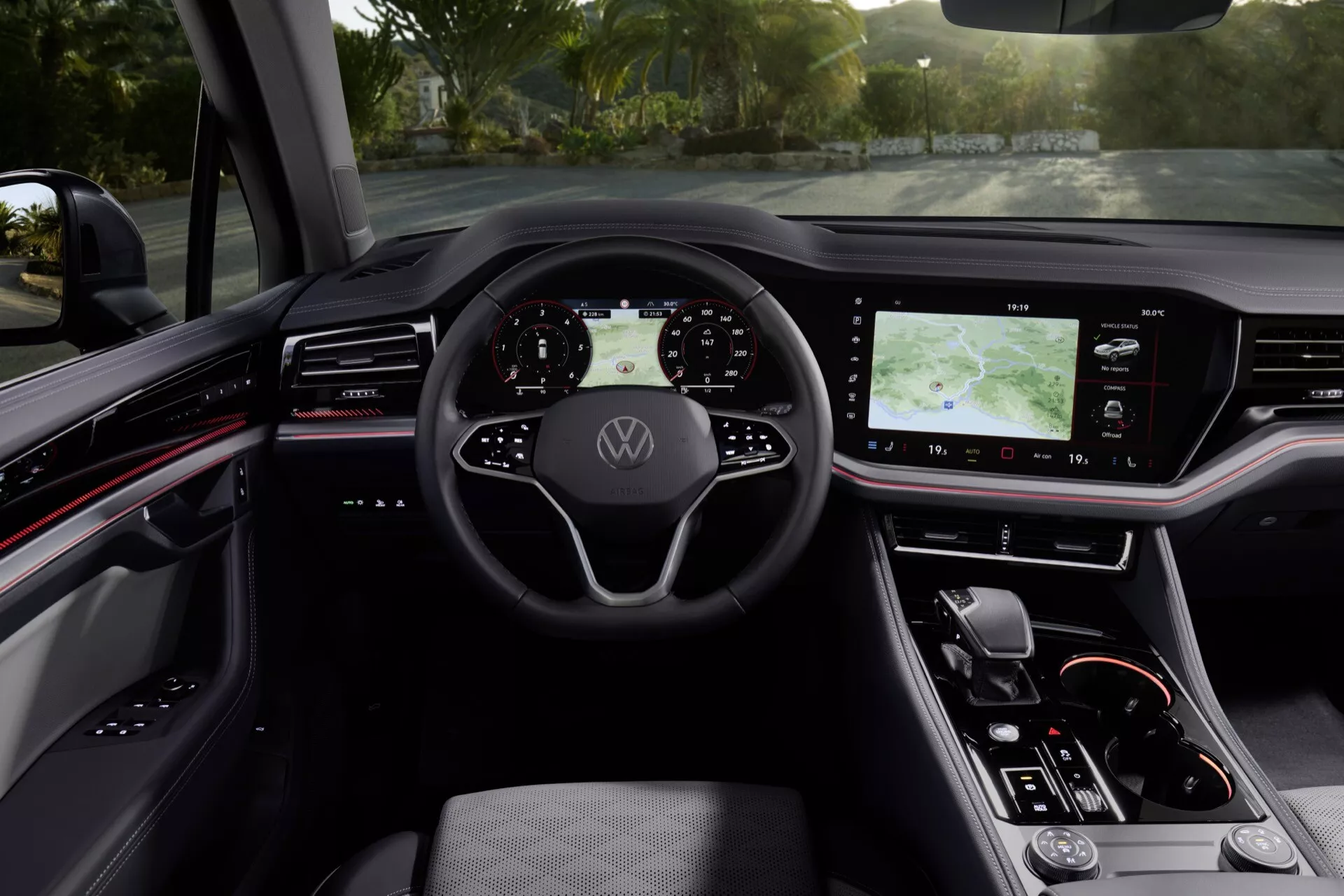 Intérieur du VW Touareg 2023 présentant un volant avec logo Volkswagen, un tableau de bord numérique, un grand système d'infodivertissement tactile sur la console centrale, un siège conducteur ergonomique en simili cuir, et des éléments de design moderne avec accents rouges du point de vue du conducteur.
