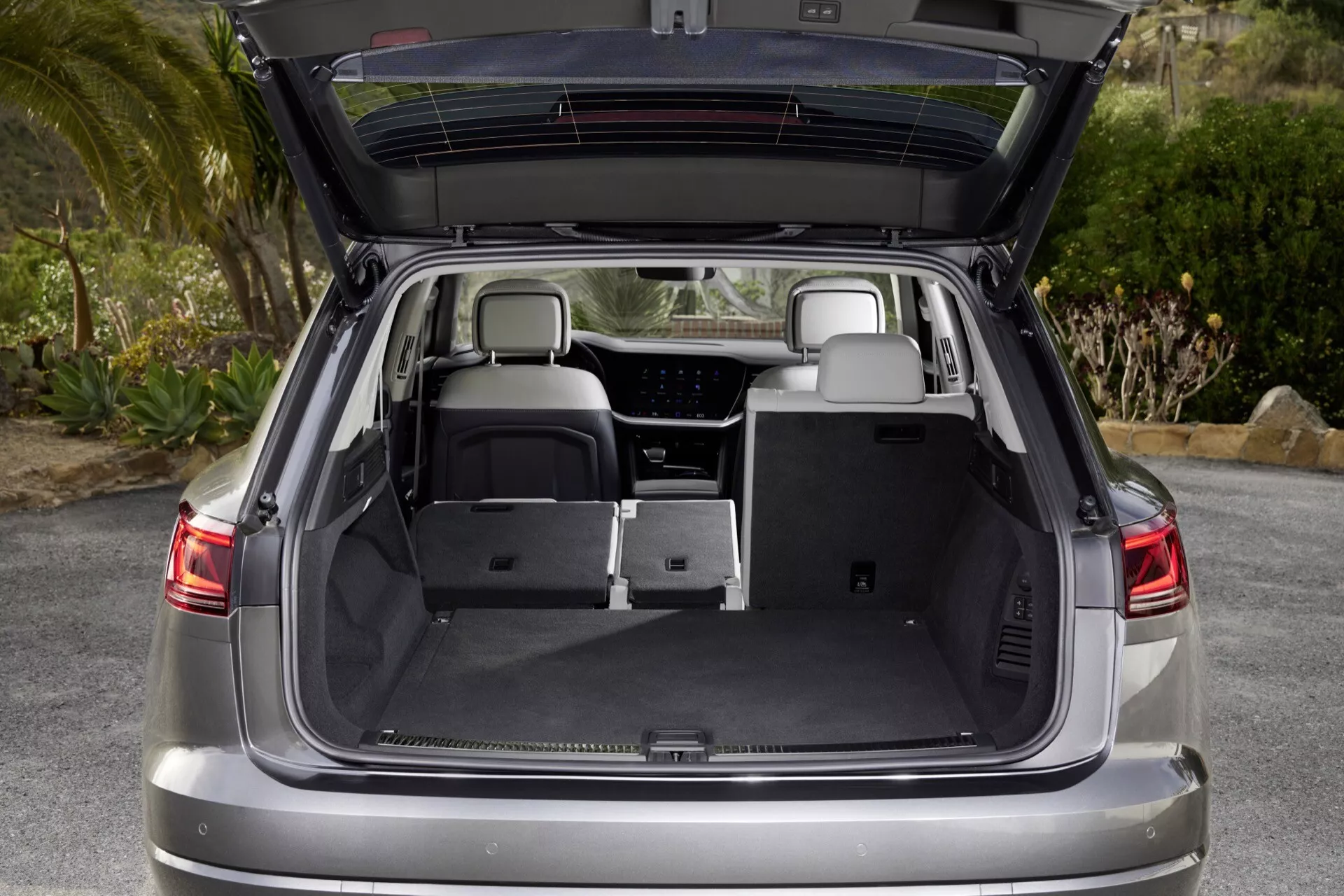 Vue arrière d'un VW Touareg 2023 (III Facelift) avec le coffre ouvert montrant un espace de chargement spacieux, des sièges arrière rabattables et des fonctionnalités intérieures modernes sous un angle biaisé.