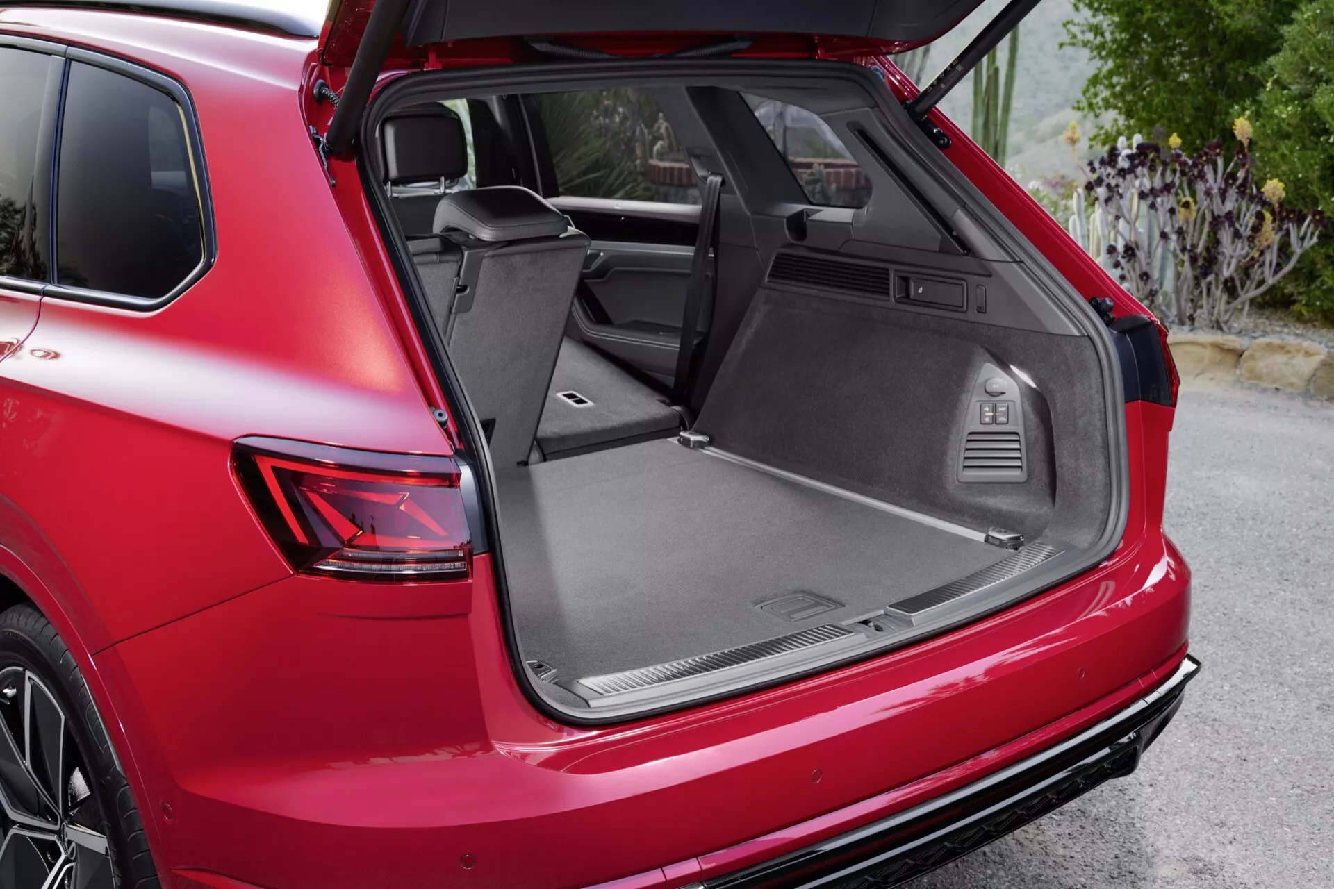 SUV rouge VW Touareg (III Facelift) 2023, vue arrière latérale en diagonale montrant coffre ouvert, côté passager arrière, feu arrière, roue en alliage, pare-chocs arrière et espace de chargement spacieux avec caractéristiques utilitaires