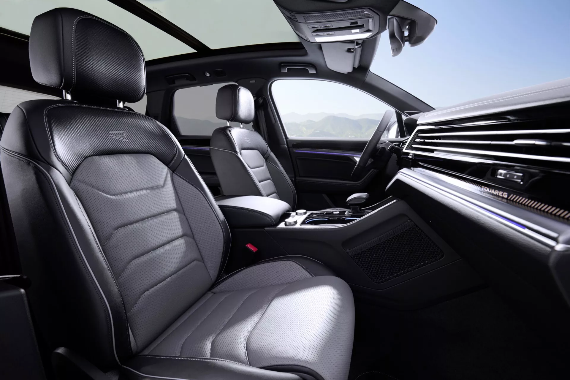 Intérieur du VW Touareg 2023 présentant des caractéristiques de luxe et de technologie telles que des sièges en cuir de haute qualité, tableau de bord en finition bois, levier de vitesse automatique, contrôle climatique bi-zone, volant multifonctions, éclairage d'ambiance de toit panoramique et console du système d'infodivertissement.