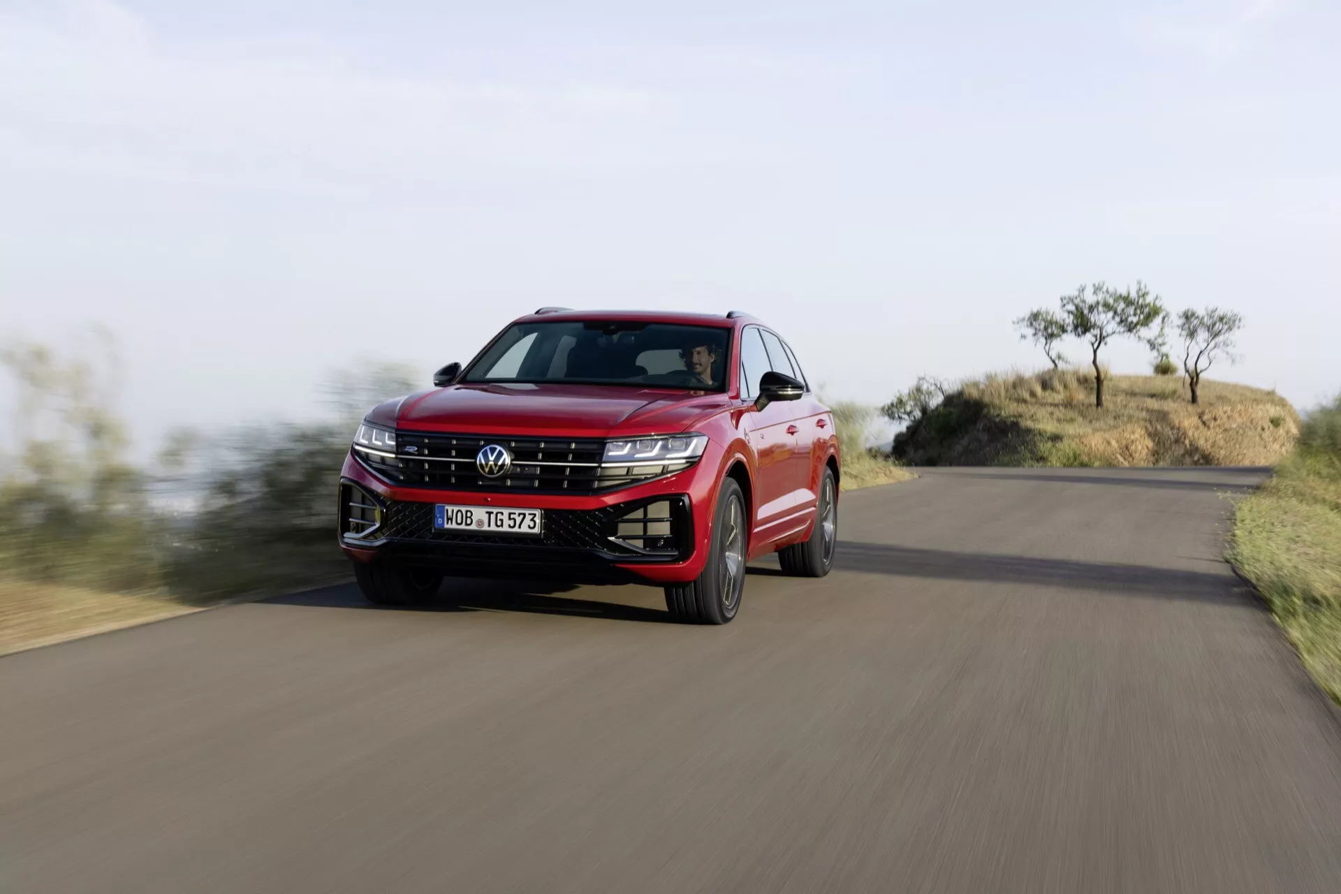 Volkswagen Touareg 2023 en rouge, capturée en mouvement depuis un angle bas mettant en lumière la grille, les phares LED, et le profil latéral dynamique au milieu d'un paysage naturel.